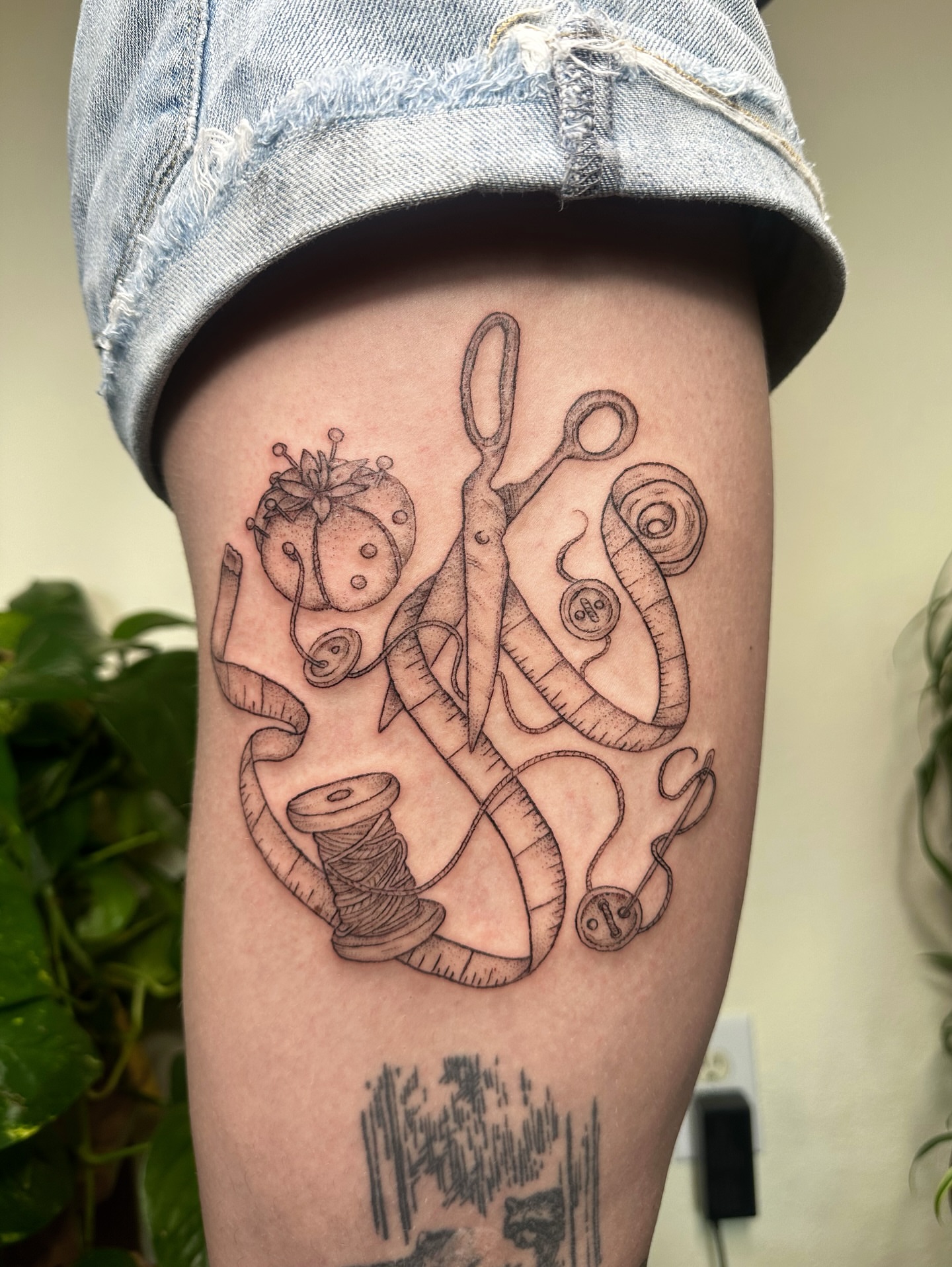 Sewing tools black and grey tattoo on the thigh by kenzie hunter