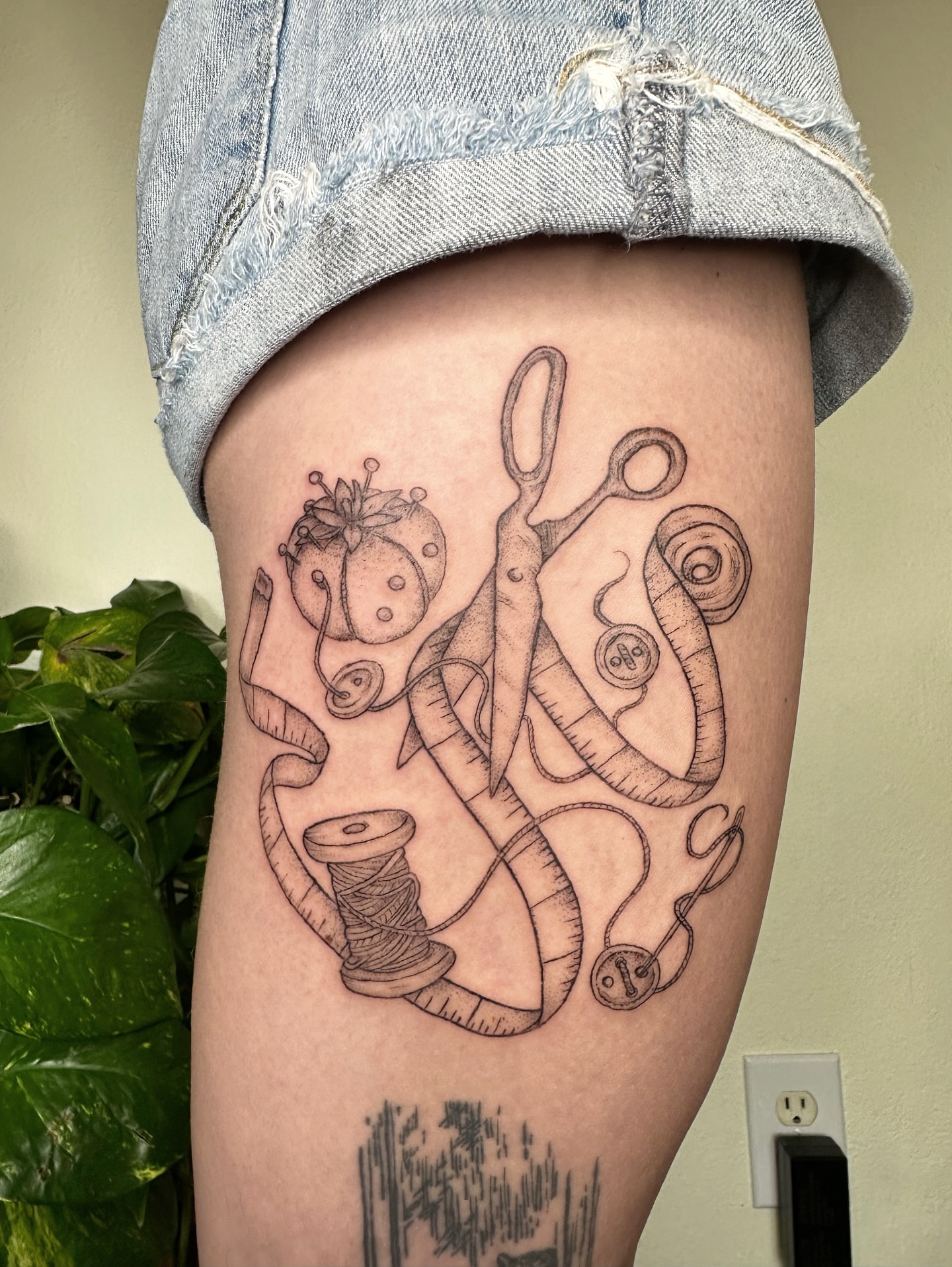 Sewing tools black and grey tattoo on the thigh by kenzie hunter