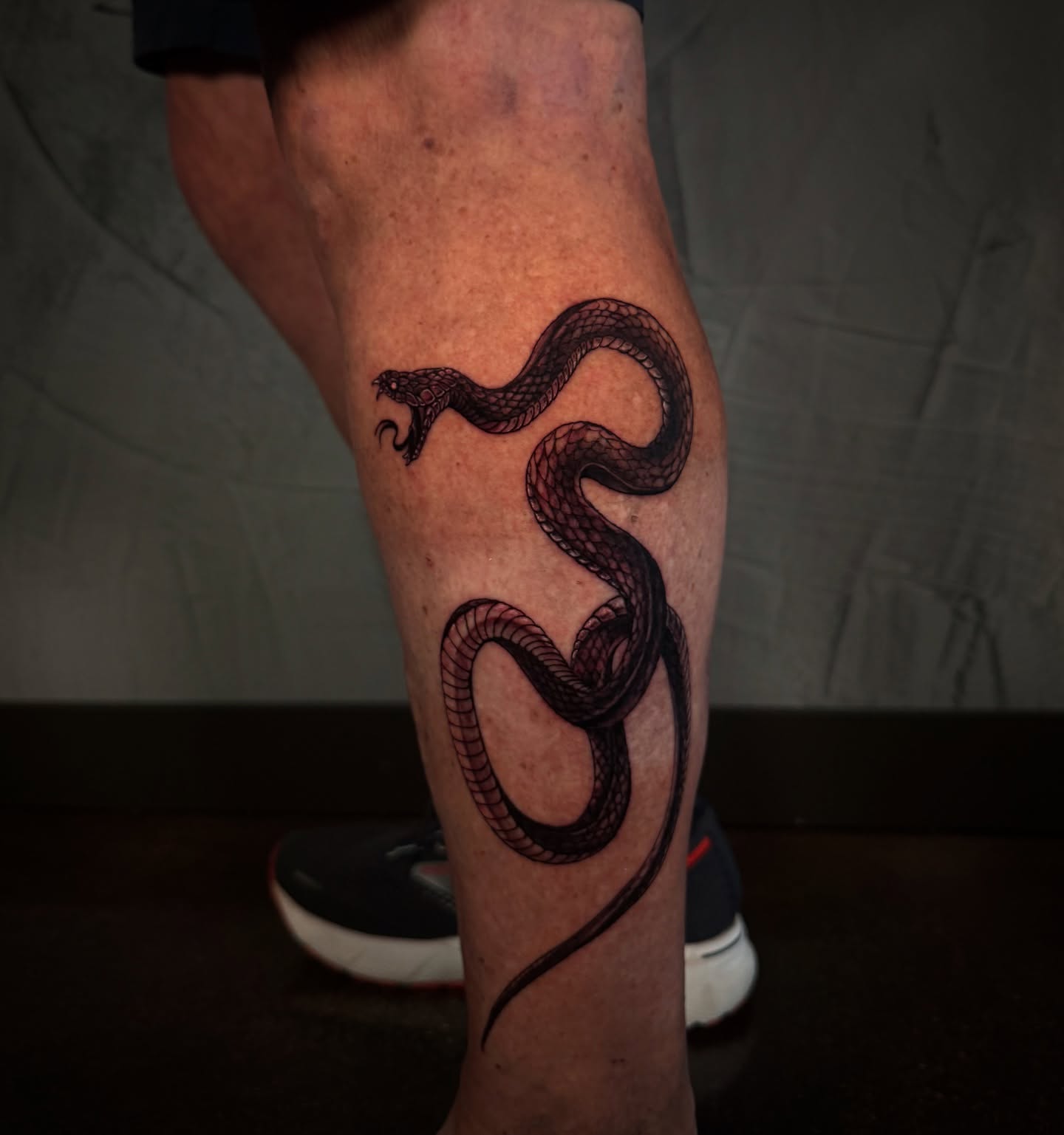 Snake black and grey tattoo on the calf by Ethan Lund