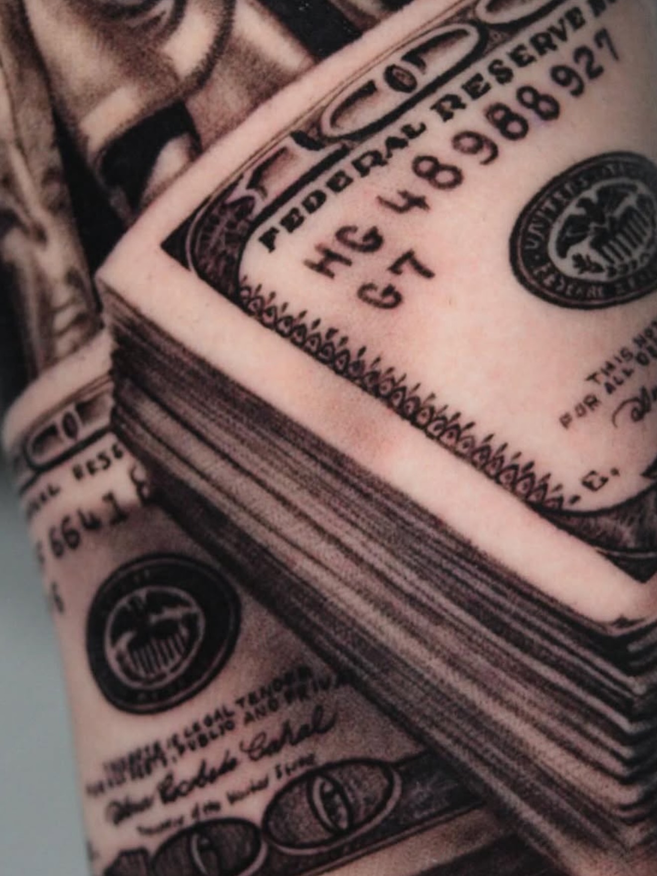Stacked dollar bills black and grey tattoo on the forearm by Sergio Mendez