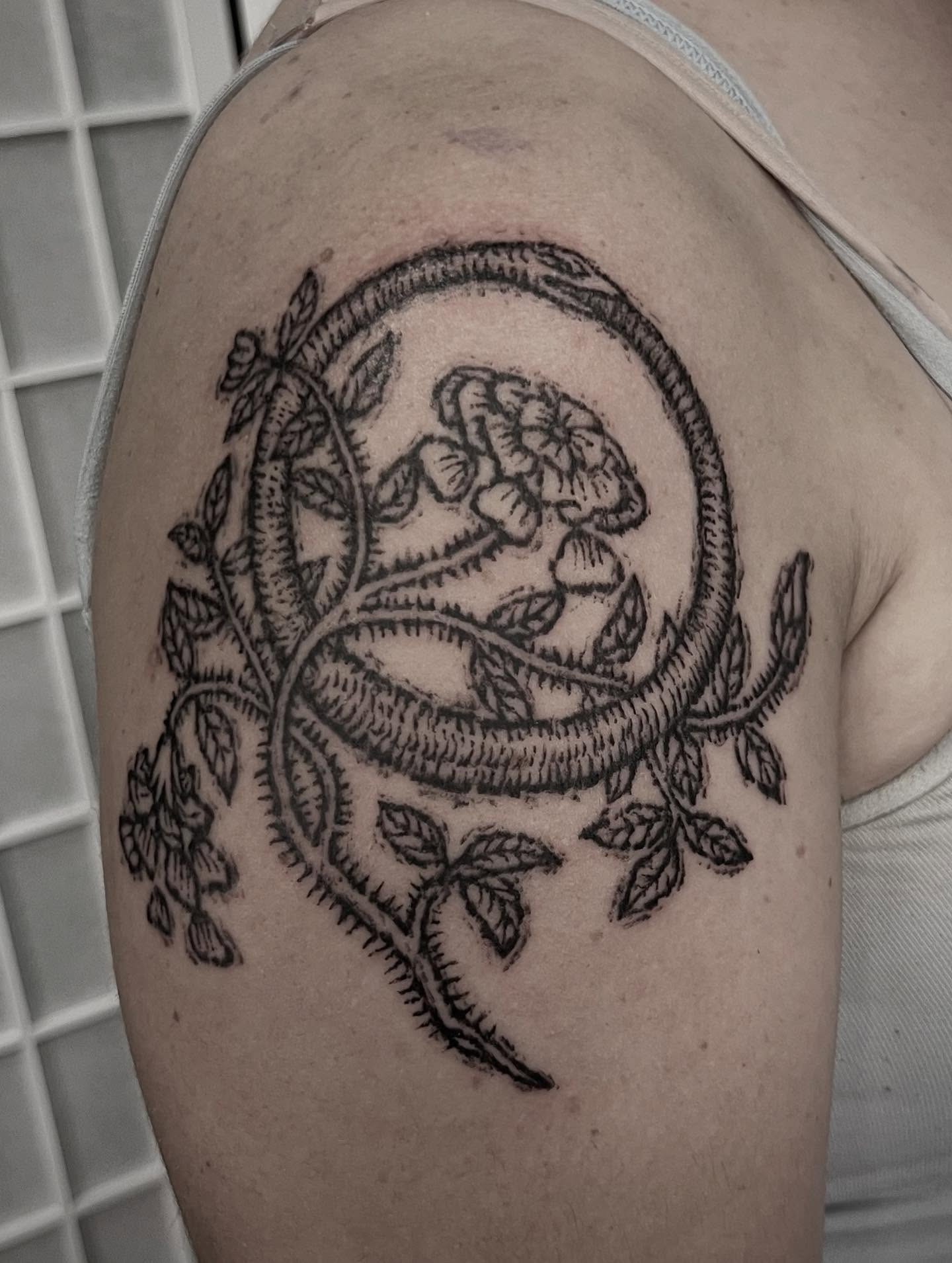 Snake and flowers black and grey tattoo on the shoulder by Tattoo Artist