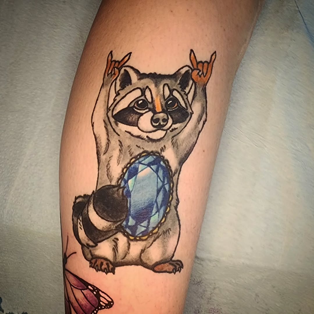 Raccoon holding a gem realism tattoo on the forearm by Karley Michelle Moody