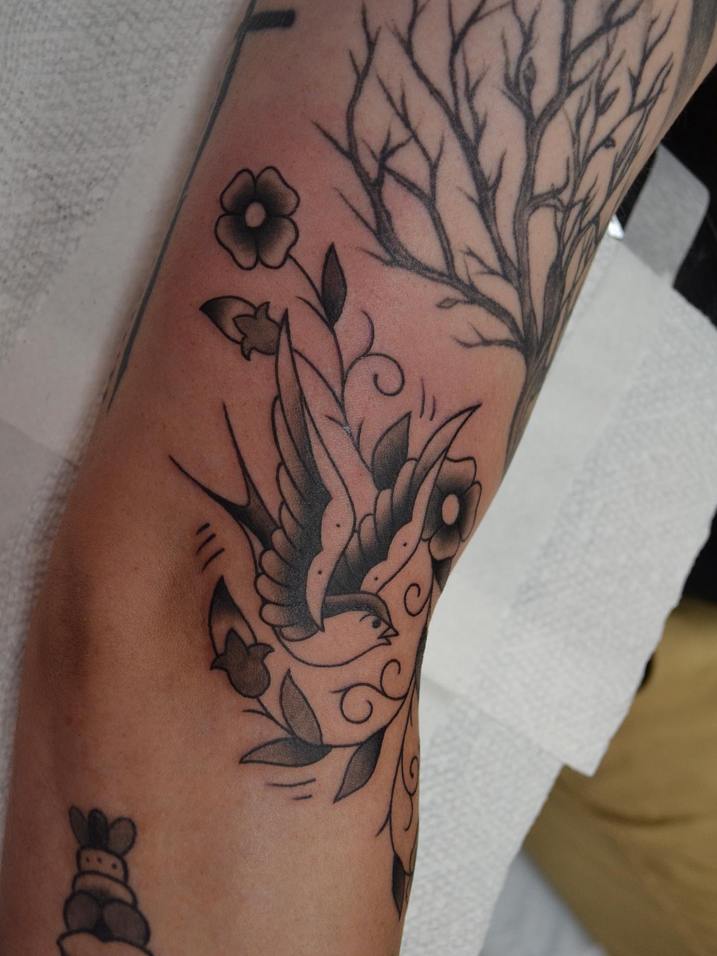 Bird and floral black and grey tattoo on the forearm by Vanessa Acosta