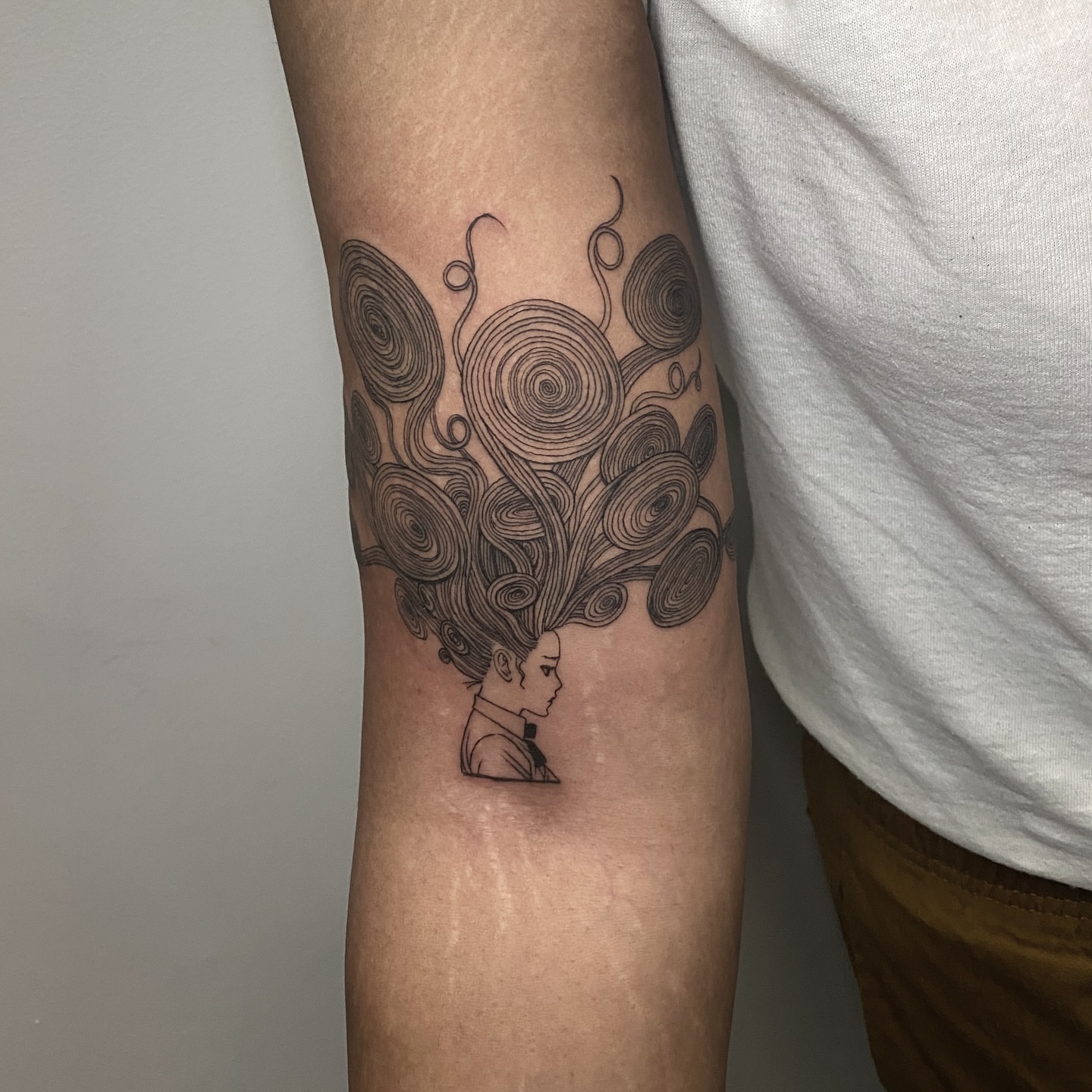 Spiraling hair black and grey tattoo on the forearm by Rowan Starr