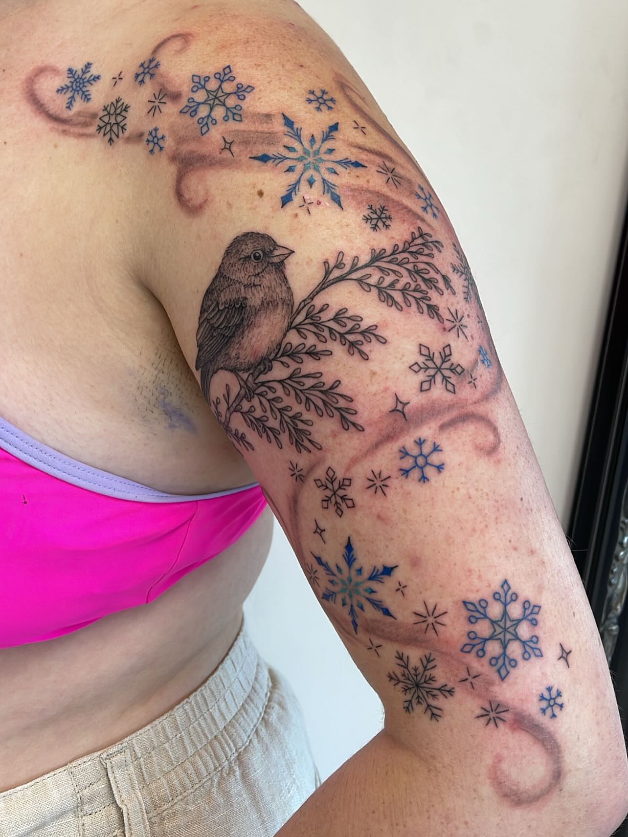 Bird and snowflakes black and grey tattoo on the upper arm by Miesha Busker