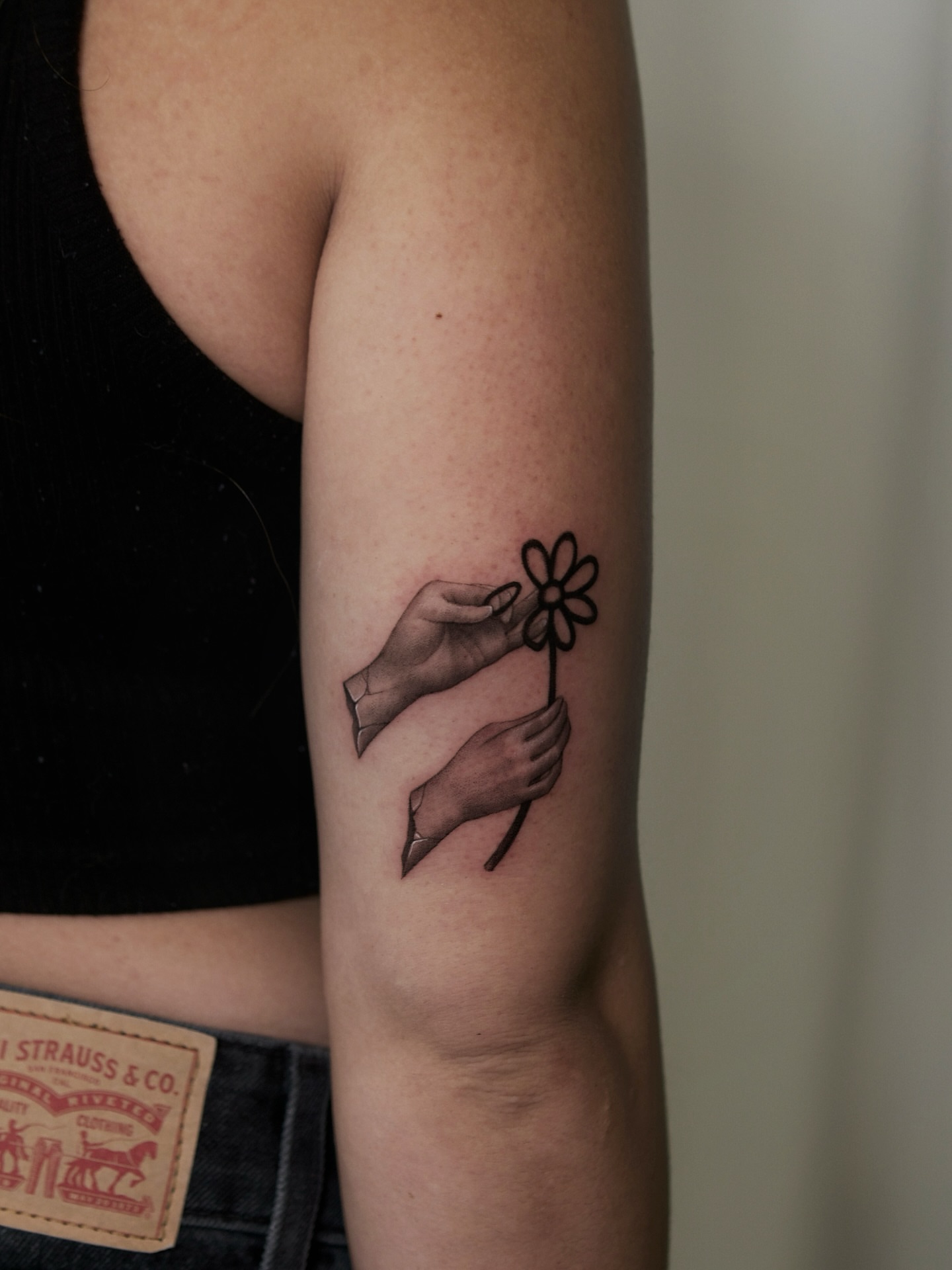 Hands holding flower black and grey tattoo on the forearm by Ray Quinday