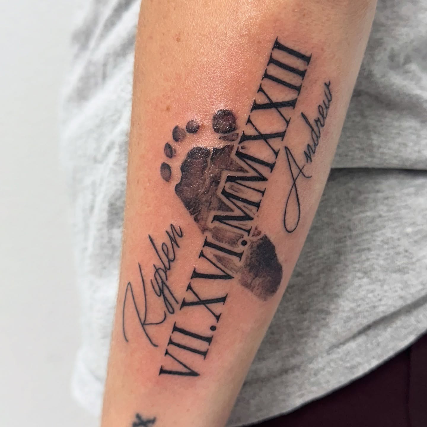 Footprint with names and date black and grey tattoo on the forearm by Lacee-Beth Finch