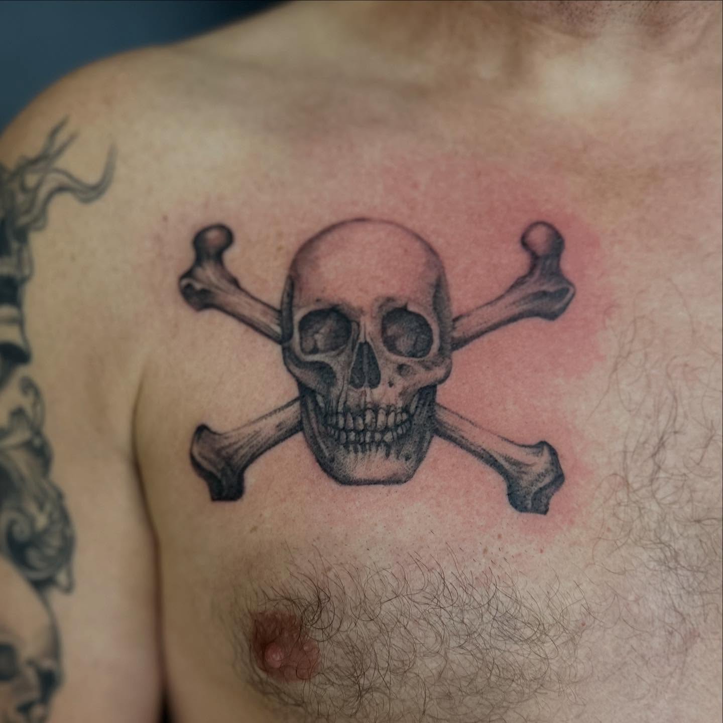 Skull and crossbones black and grey tattoo on the chest by Emma