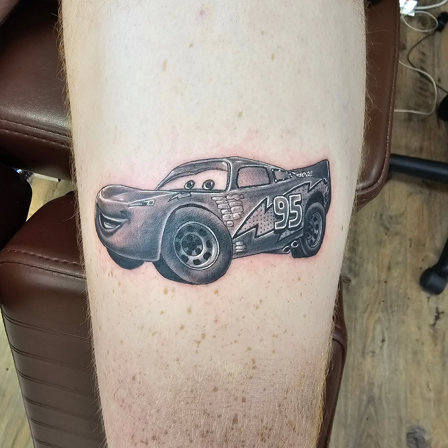 Lightning mcqueen black and grey tattoo on the thigh by Derek Davis