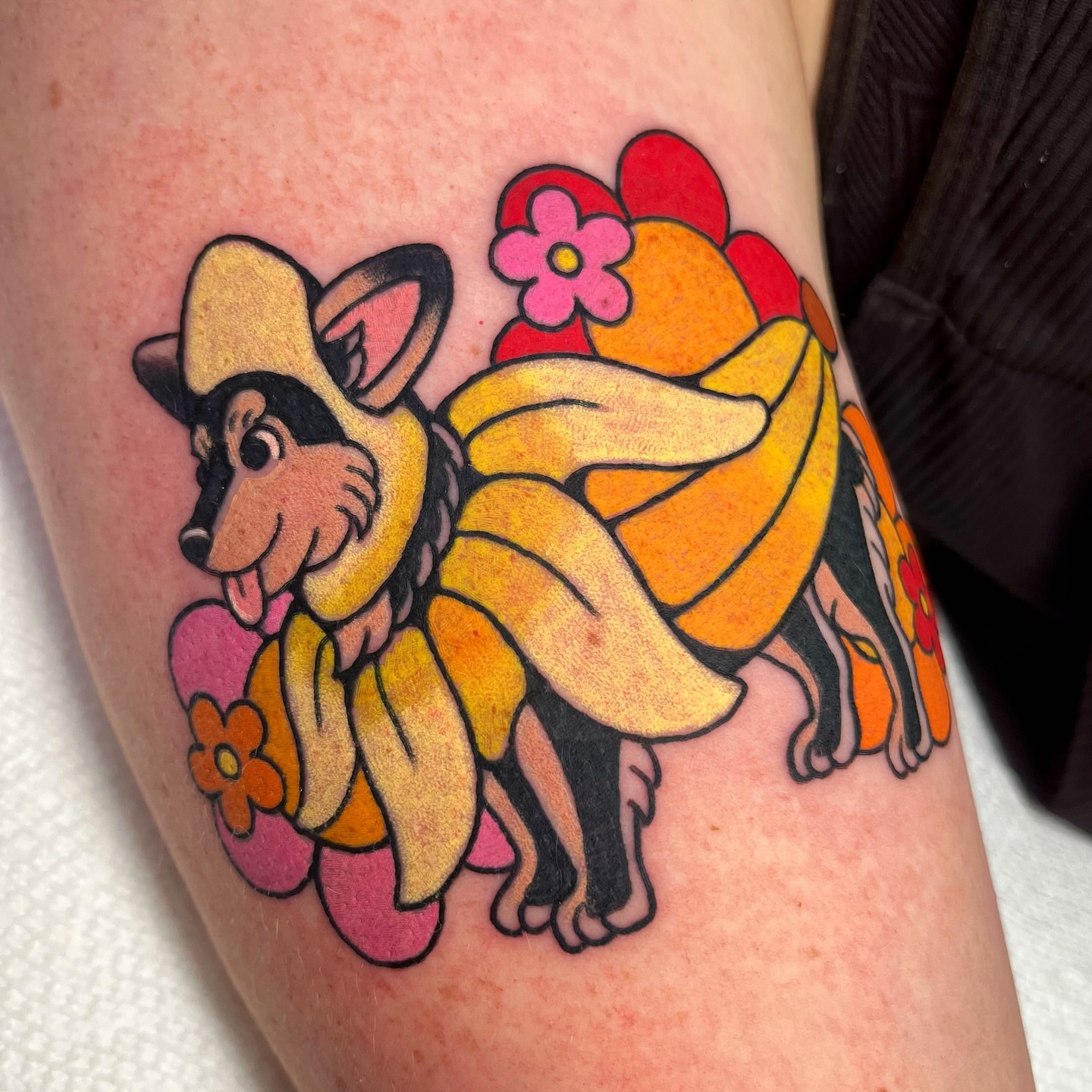 Dog wearing bananas new school tattoo on the upper arm by Alena McDonald