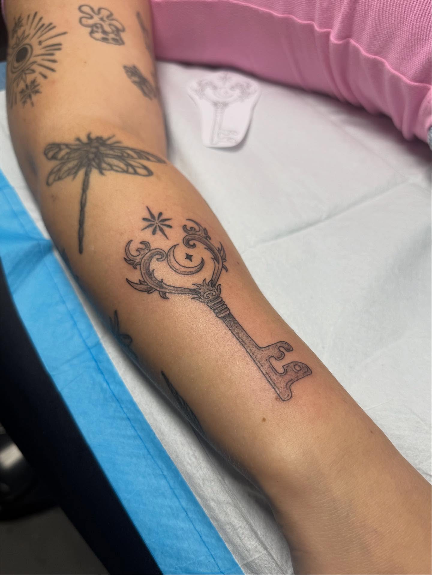 Key with floral ornament black and grey tattoo on the forearm by Maddie Jo DeYoung