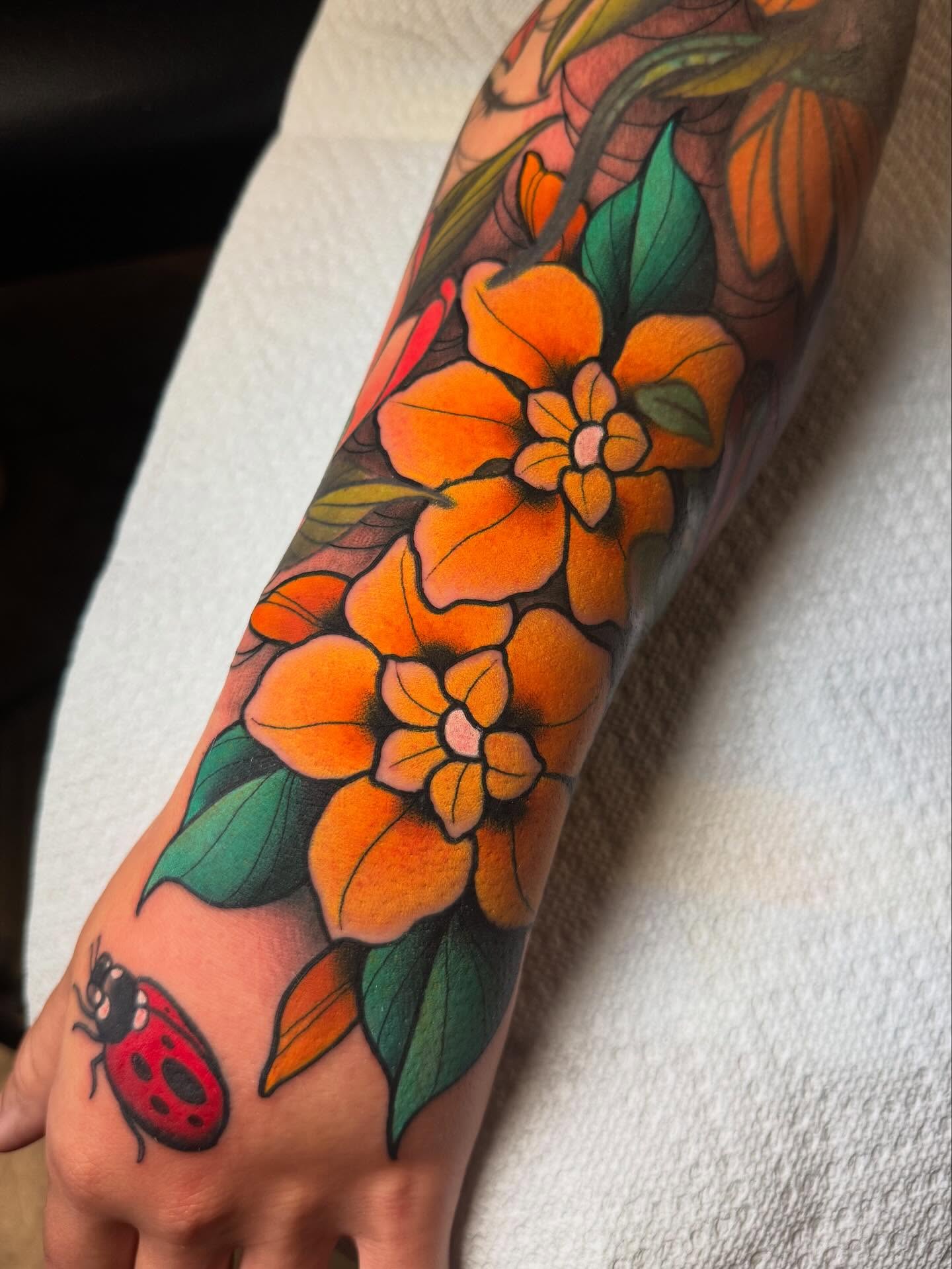 Orange flowers new school tattoo on the forearm by Jess Longfield, Des Moines, Iowa