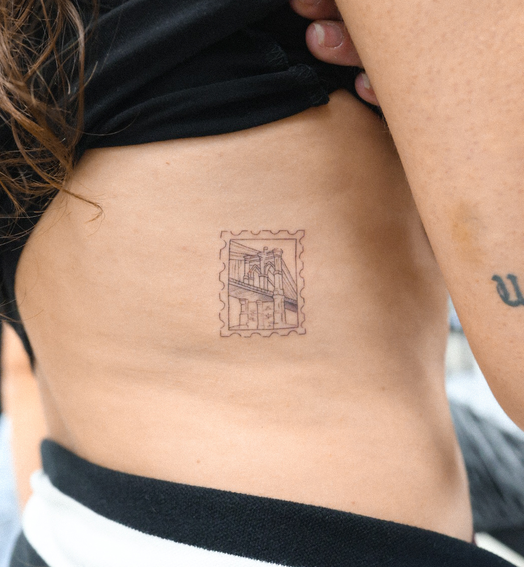 Brooklyn Bridge stamp minimalist tattoo on the torso by Fine Line, New York, New York
