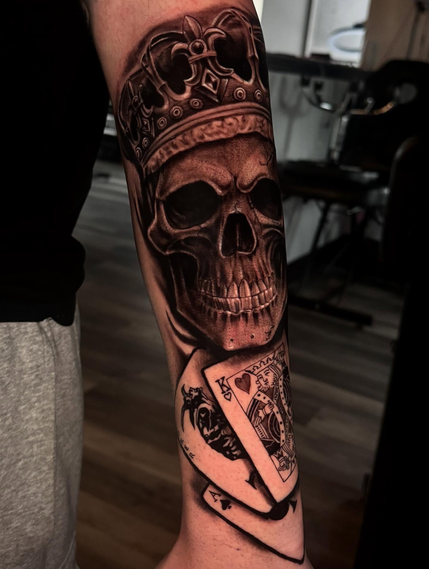 Skull and playing card realism tattoo on the forearm by Miguel Garcia