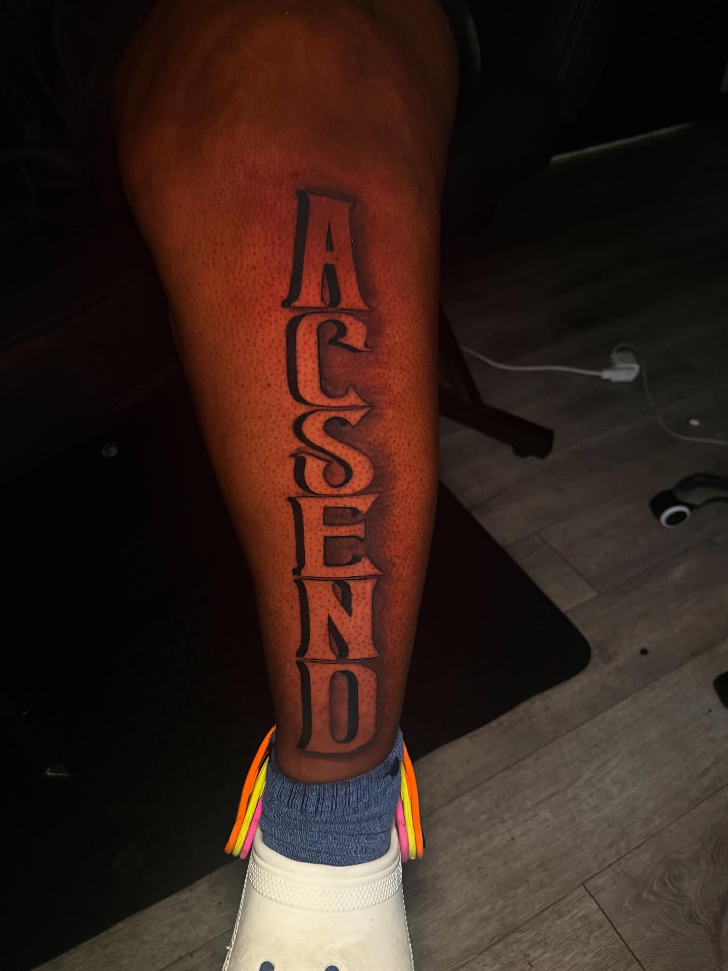 Ascend lettering script tattoo on the leg by The Ink Guru.