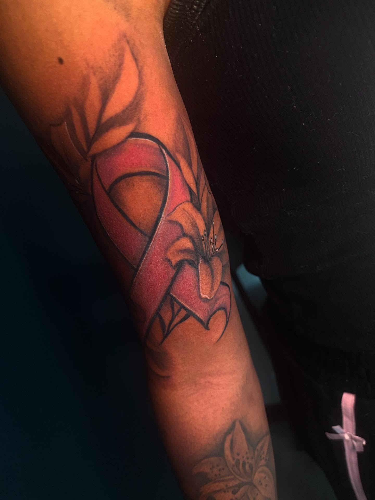 Red ribbon and lily realism tattoo on the forearm by The Ink Guru.