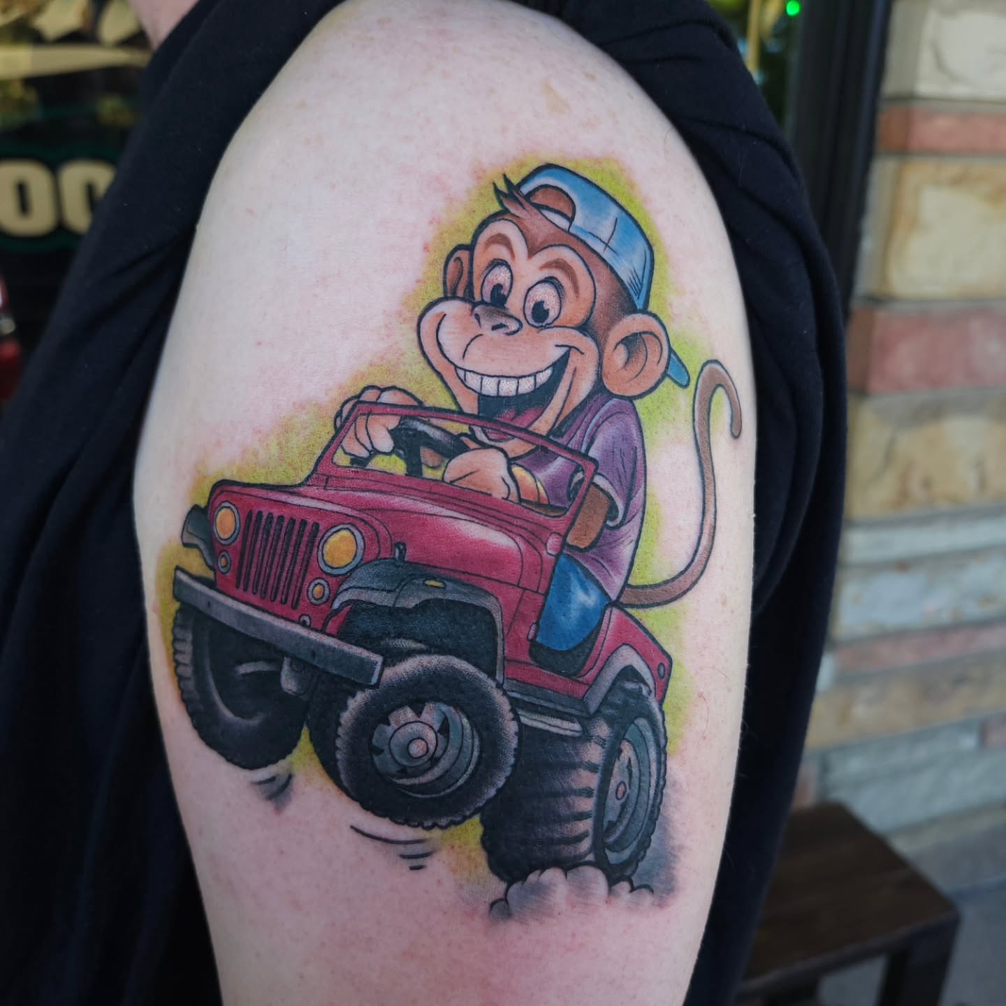 Monkey driving jeep illustrative tattoo on the upper arm by Chris Wodarski
