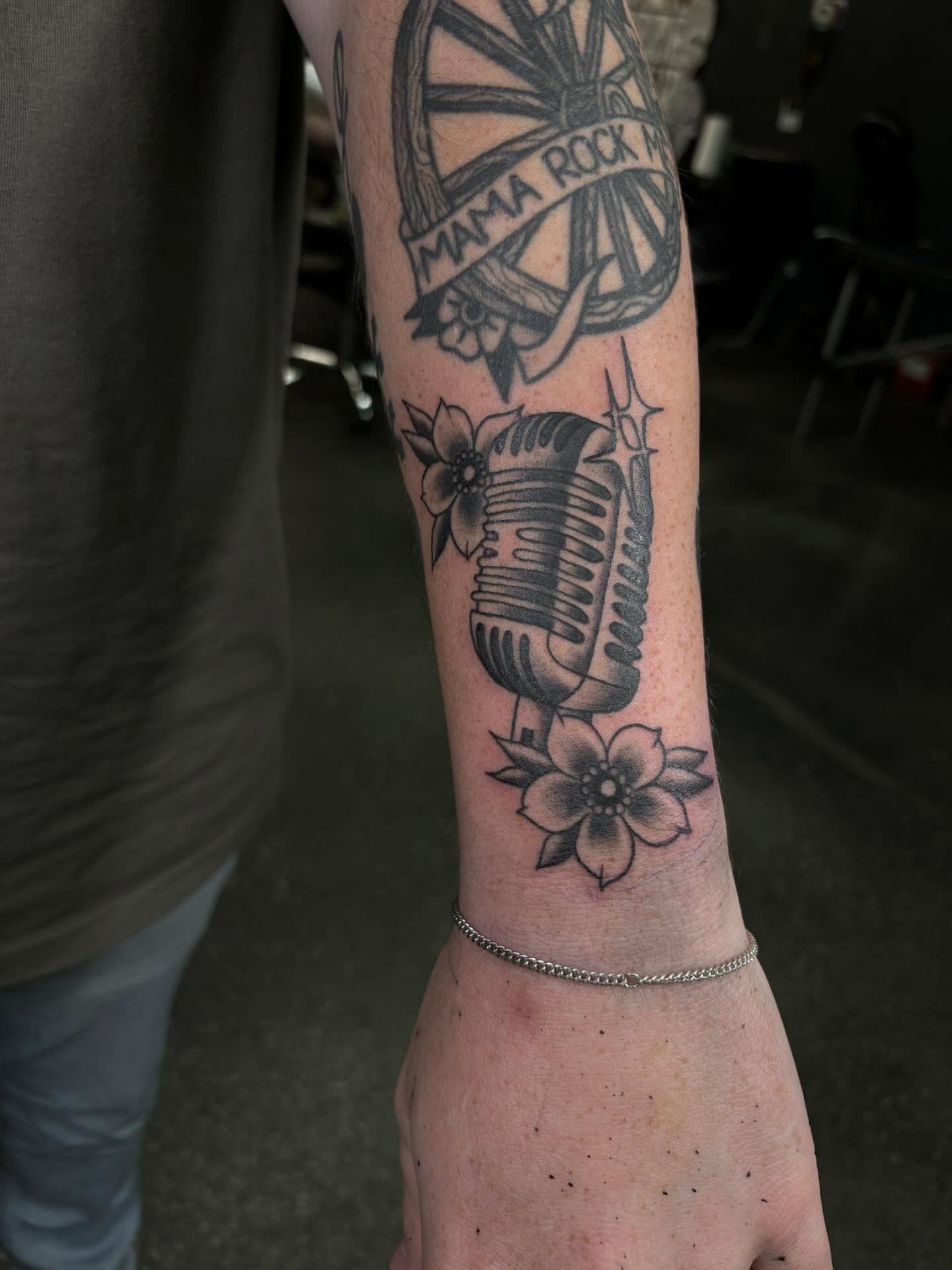 Microphone and flowers black and grey tattoo on the forearm by Brett Ferguson