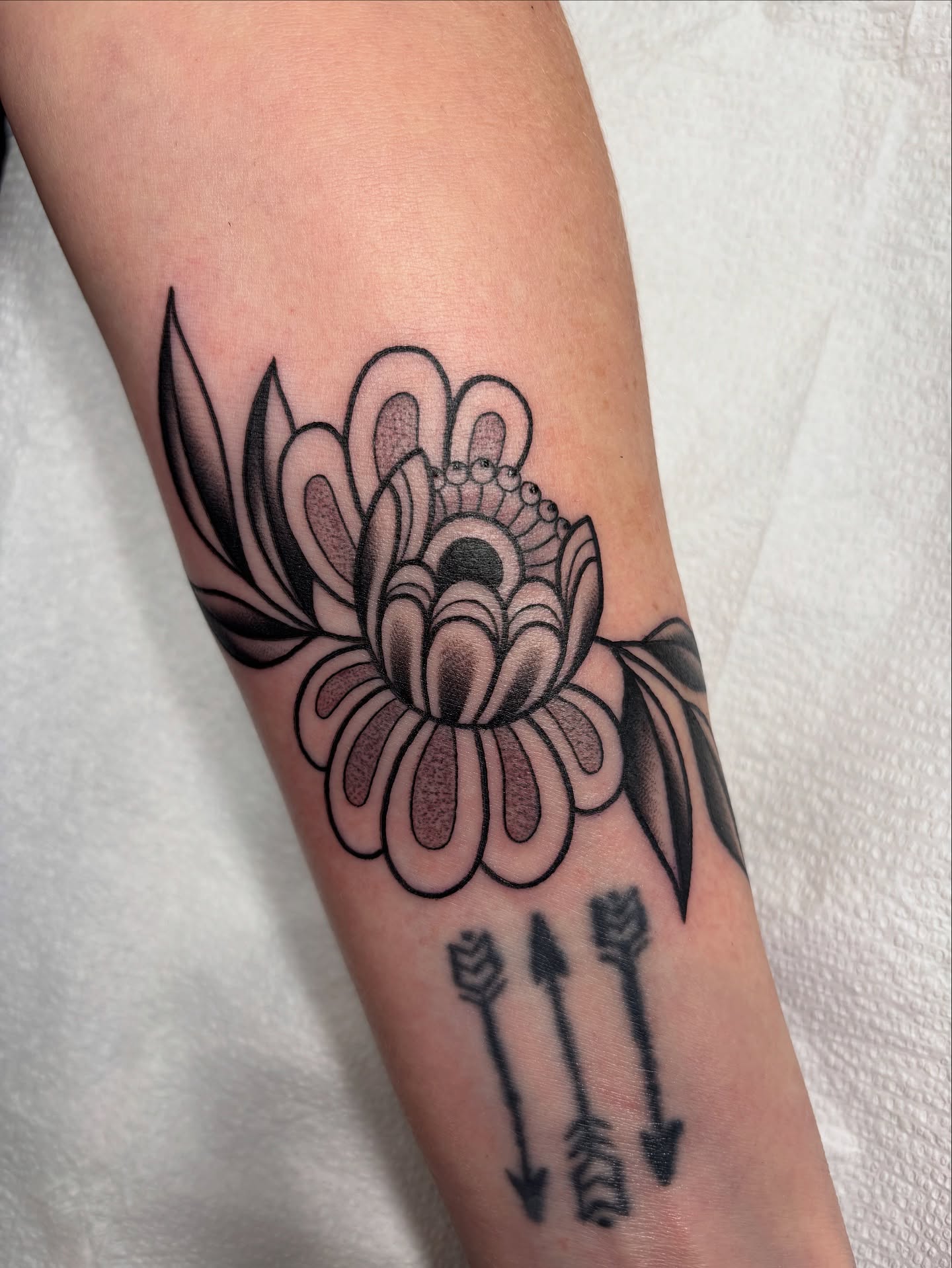Flower with arrows black and grey tattoo on the forearm by Victoria Bacon