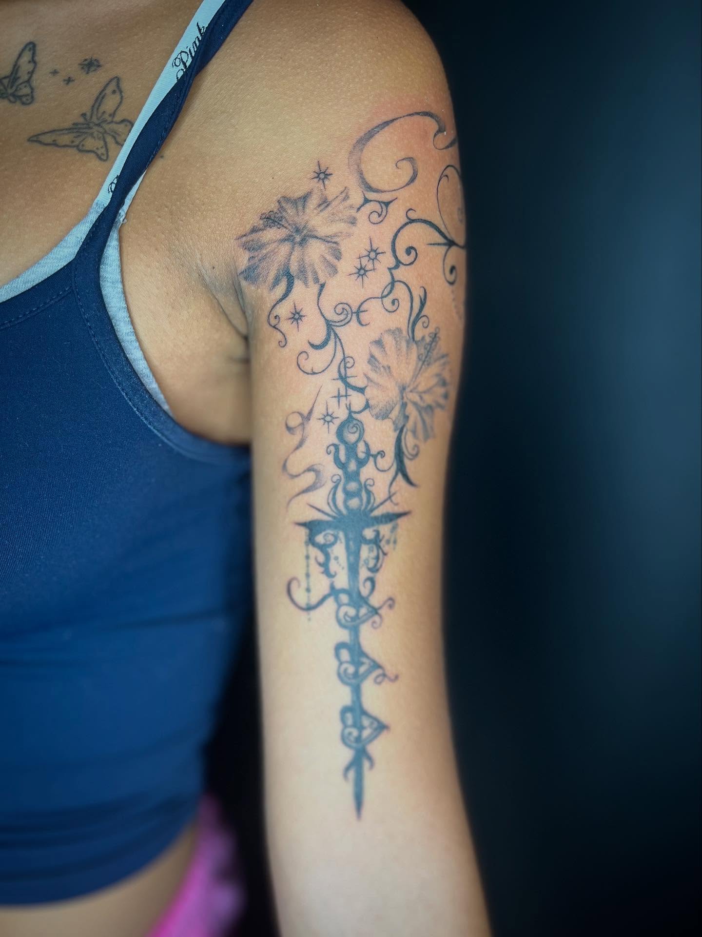 Cross with floral motifs black and grey tattoo on the upper arm by zoe? tattoo artist¿