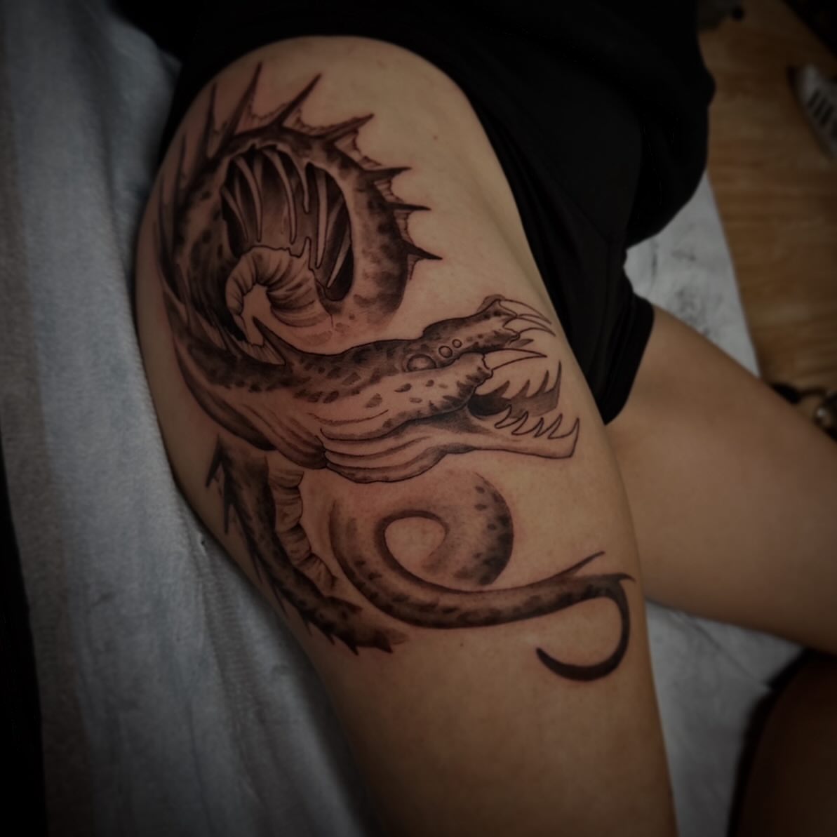 Dragon black and grey tattoo on the thigh by Sebastian Livingston