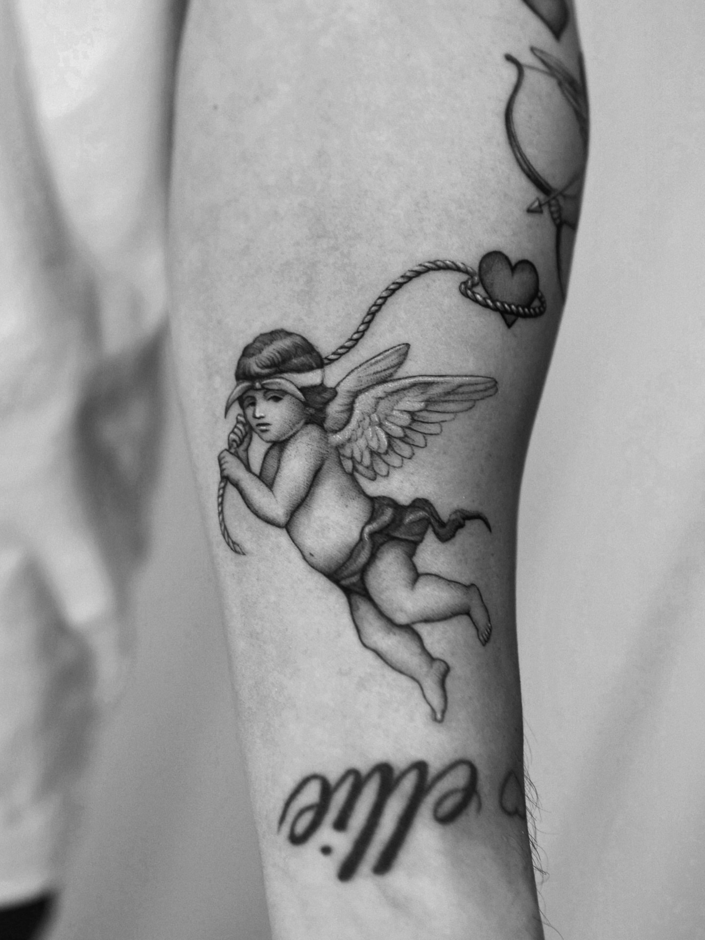 Cherub with bow black and grey tattoo on the forearm by Ray Quinday
