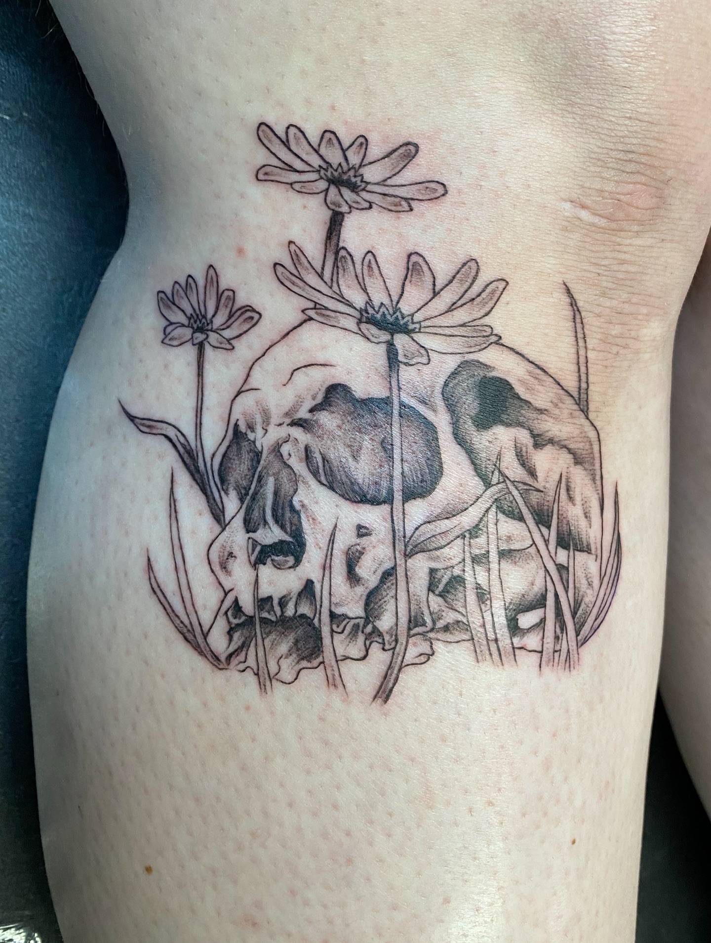 Skull and flowers black and grey tattoo on the thigh by Mack ๐ Utah Tattoos