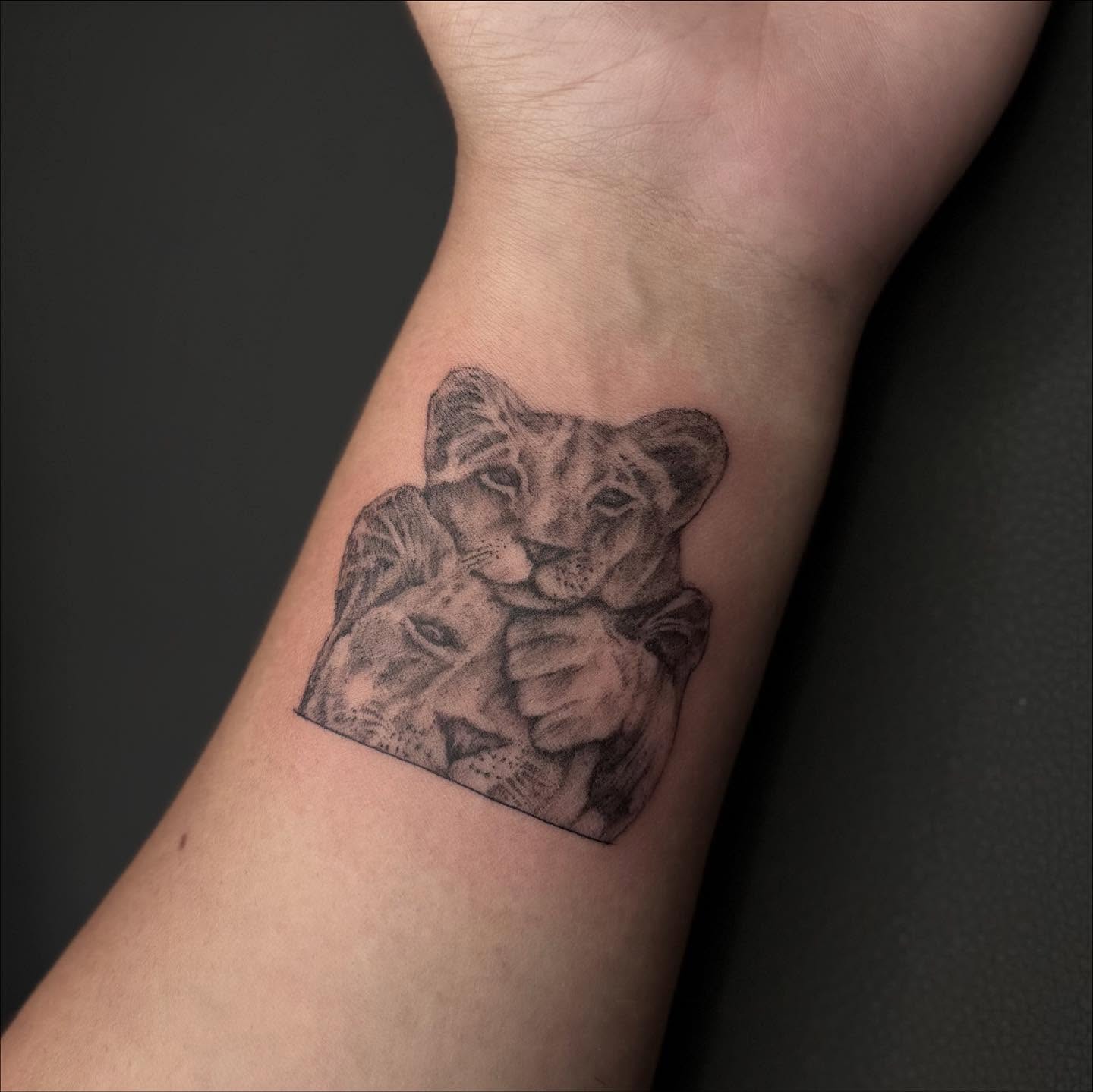 Lion cubs black and grey tattoo on the forearm by Jocelyn
