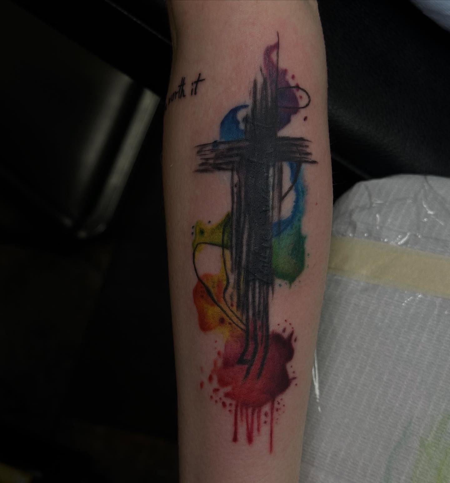 Cross with watercolor splashes watercolor tattoo on the forearm by Elizabeth Tabler