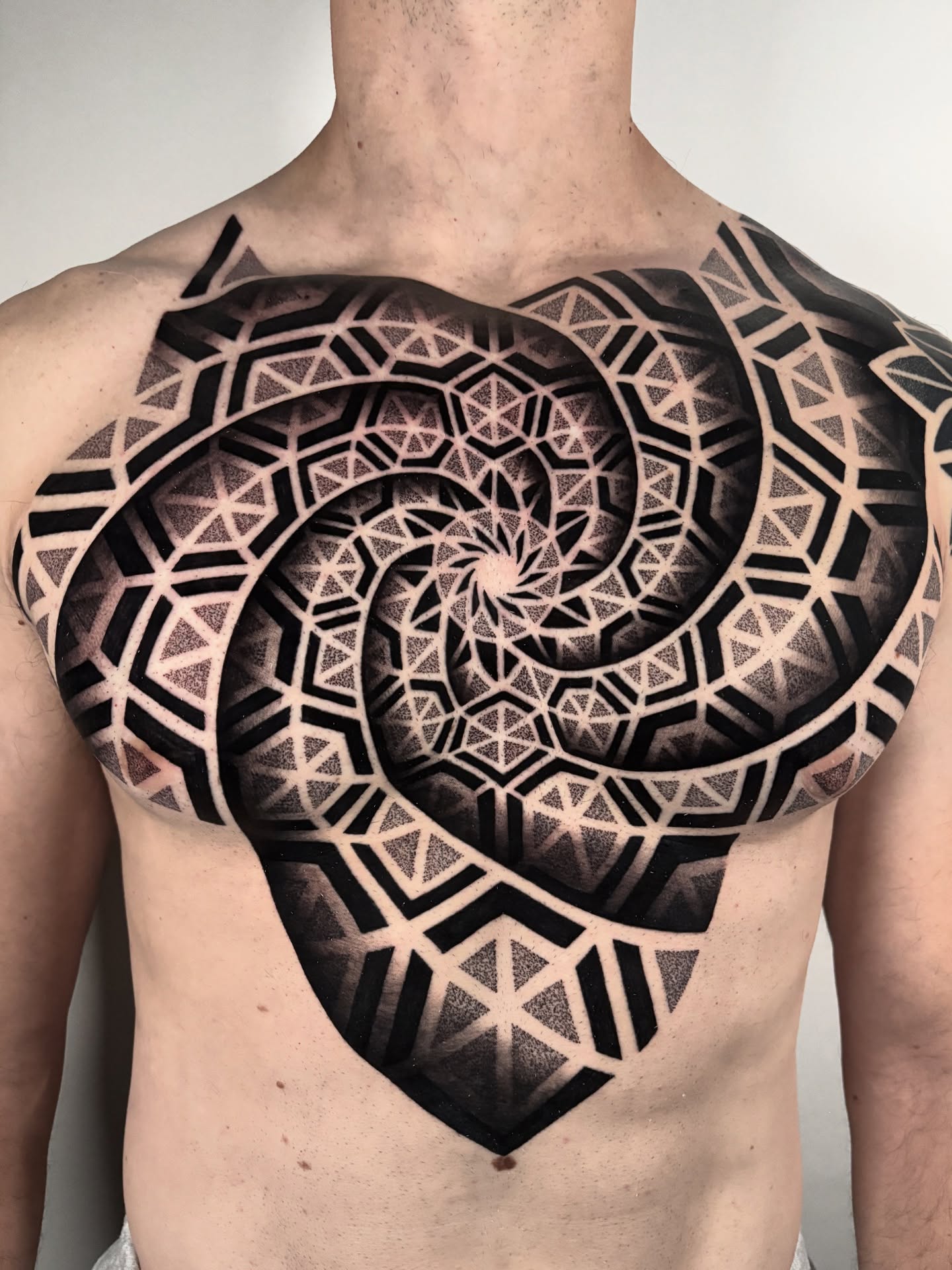 Geometric spiral dotwork tattoo on the chest by Mitch Koch