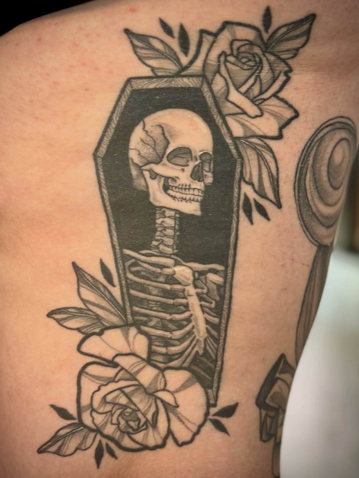 Skeleton in coffin black and grey tattoo on the thigh by Maddie Morrill