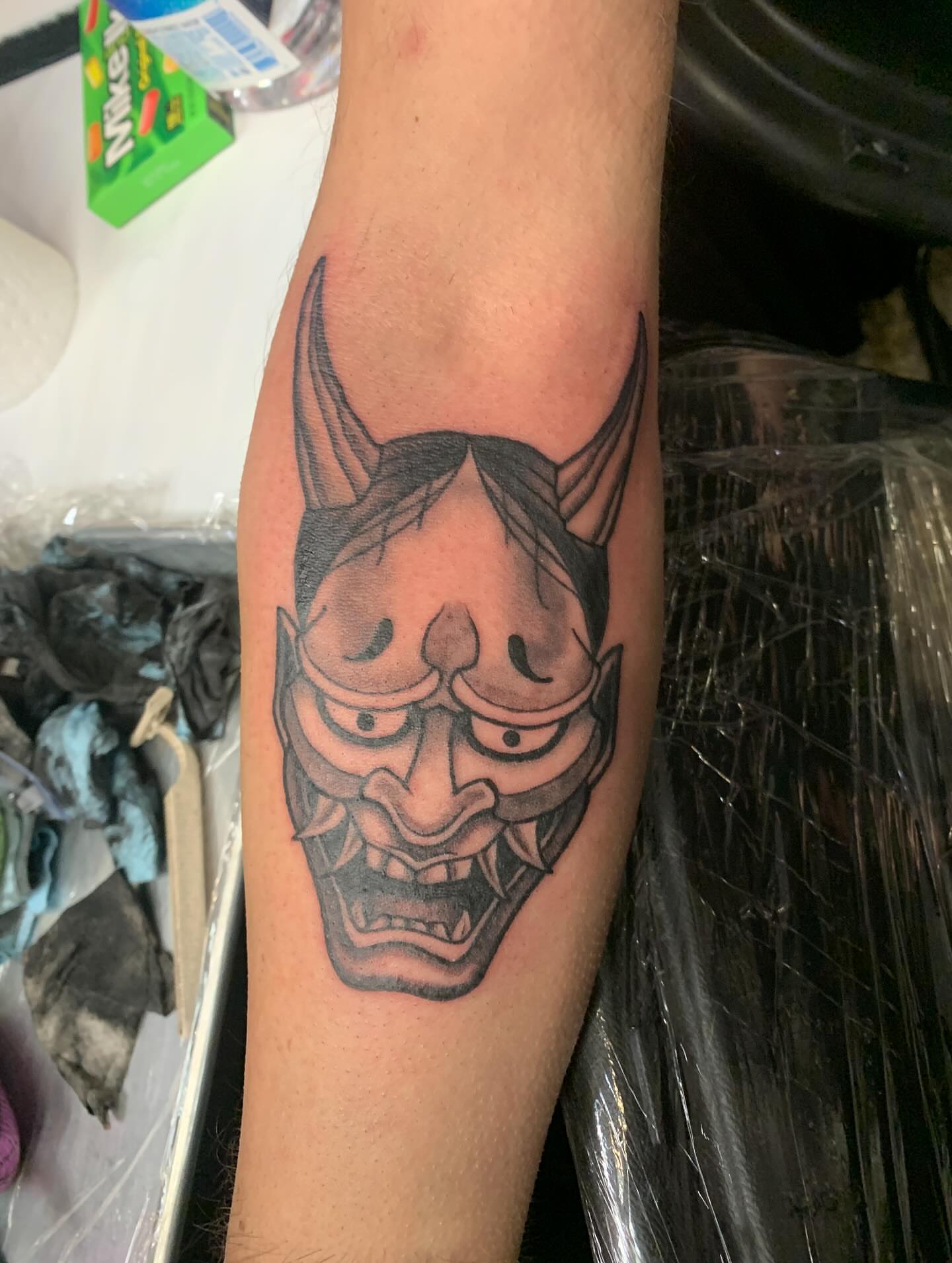 Demon mask black and grey tattoo on the forearm by Devon