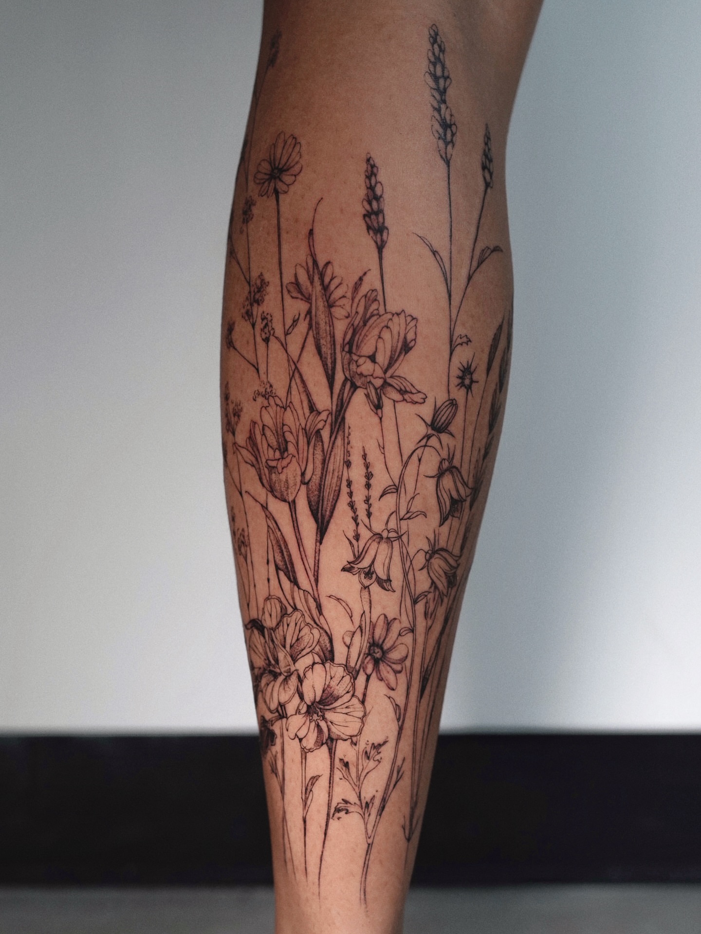 Floral bouquet black and grey tattoo on the calf by @katuvetattoo