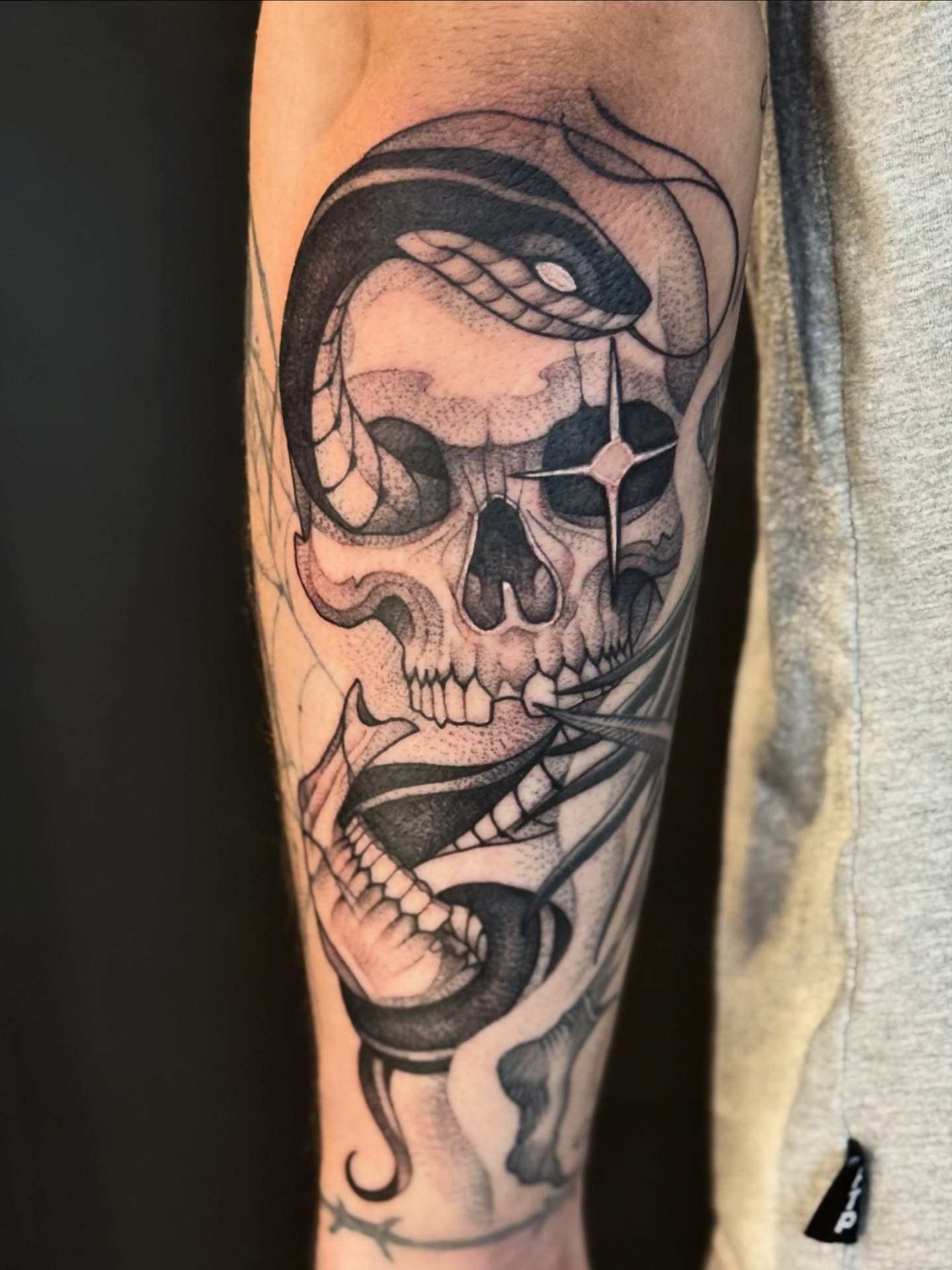 Skull with snake geometric tattoo on the forearm by Miles Romero Smith