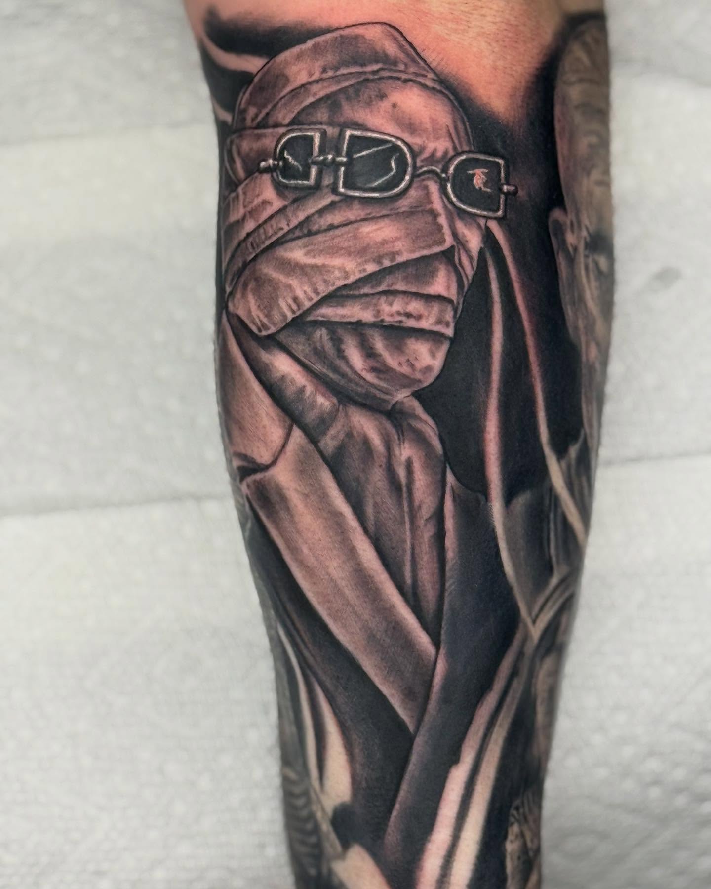 Mask-wearing figure realism tattoo on the forearm by Frank DeMao