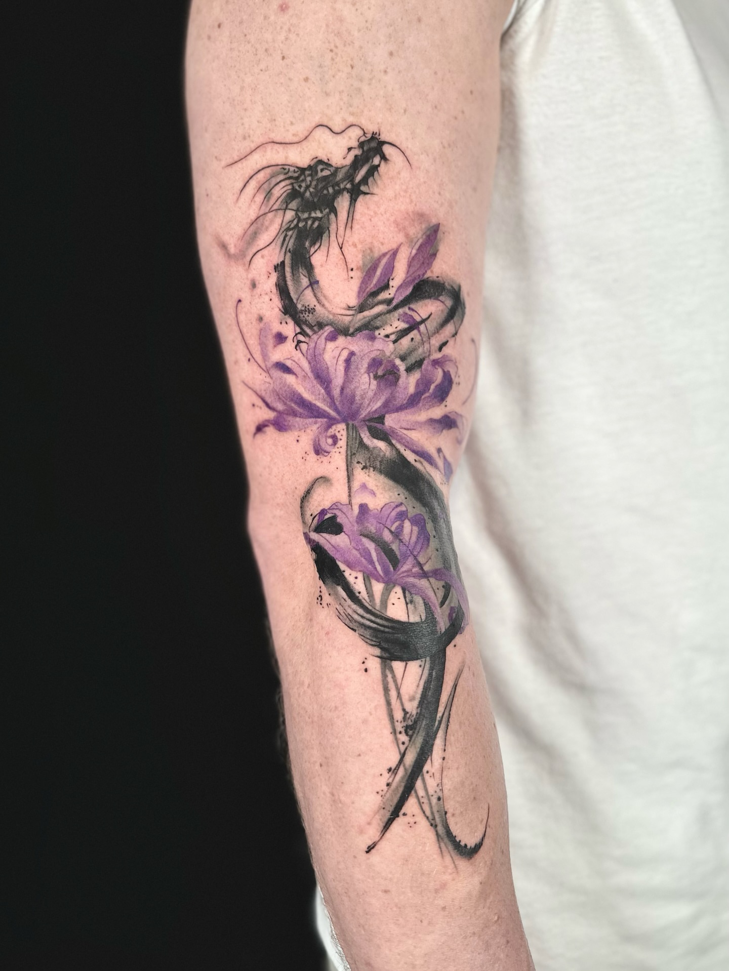 Purple flowers and dragon watercolor tattoo on the forearm by Abi