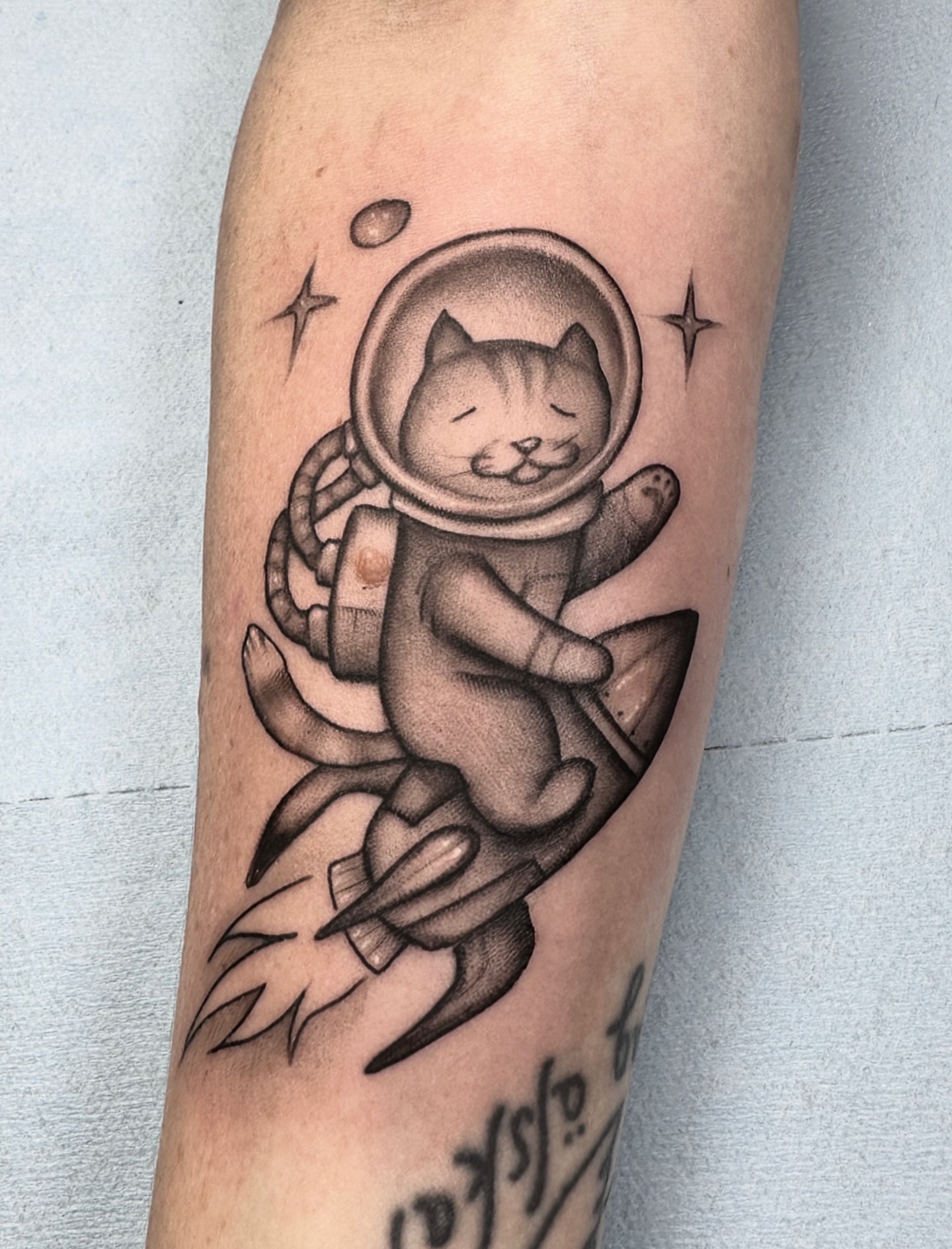 Cat astronaut black and grey tattoo on the forearm by Lawrence Edwards