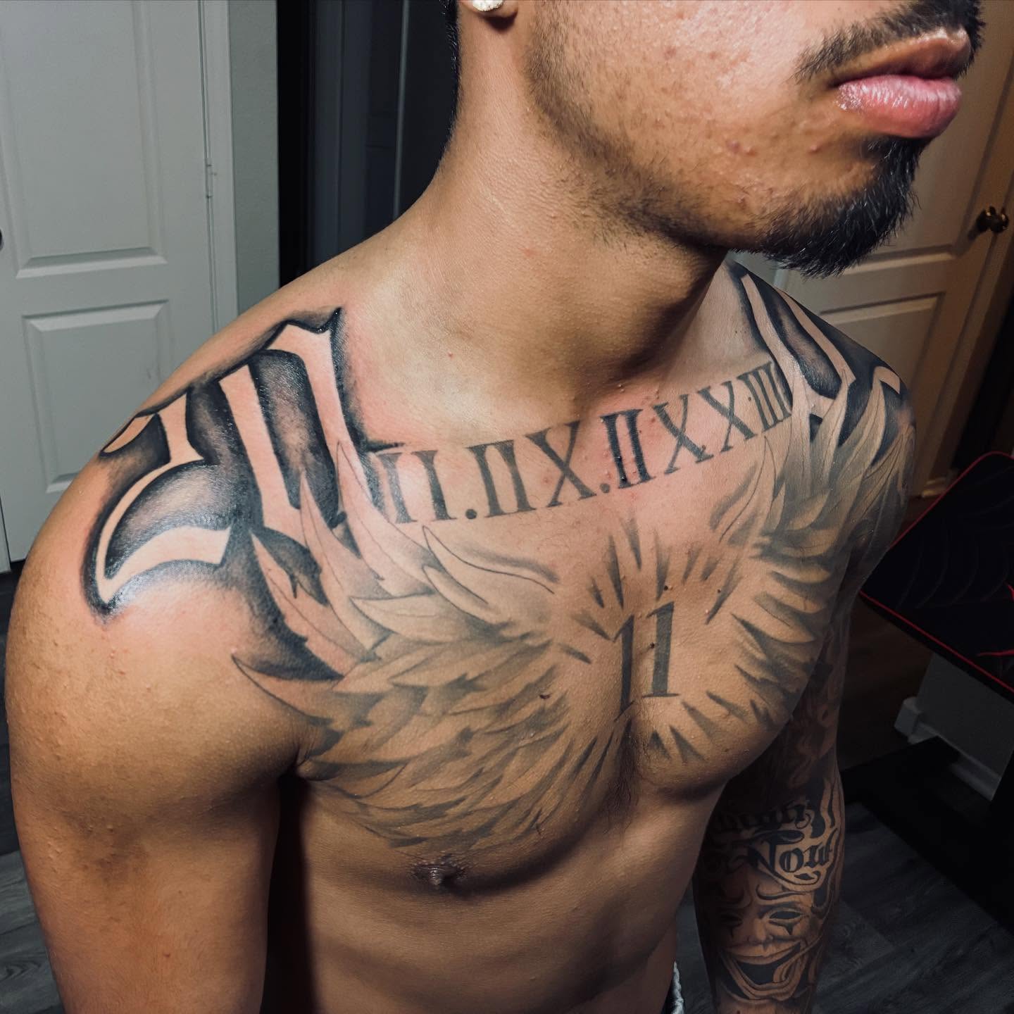 Roman numerals and wings black and grey tattoo on the chest by Nessa, Las Vegas, Nevada
