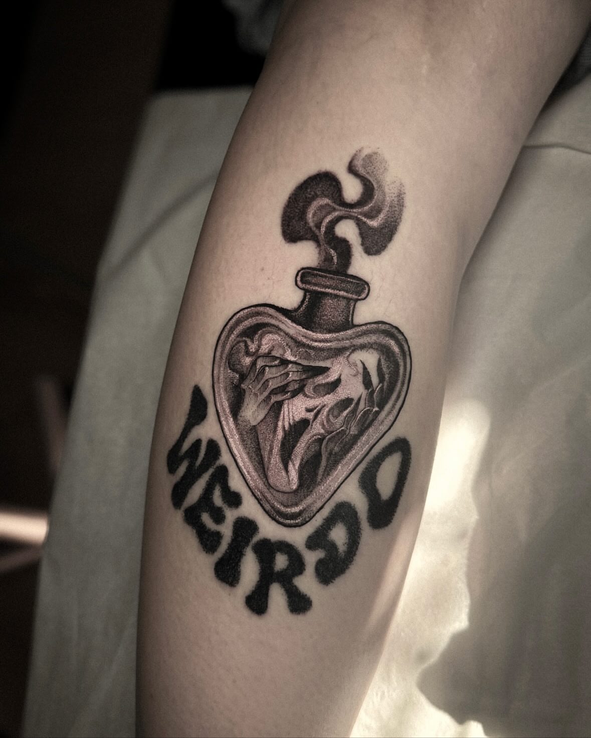 Heart-shaped potion bottle black and grey tattoo on the forearm by La Hyene