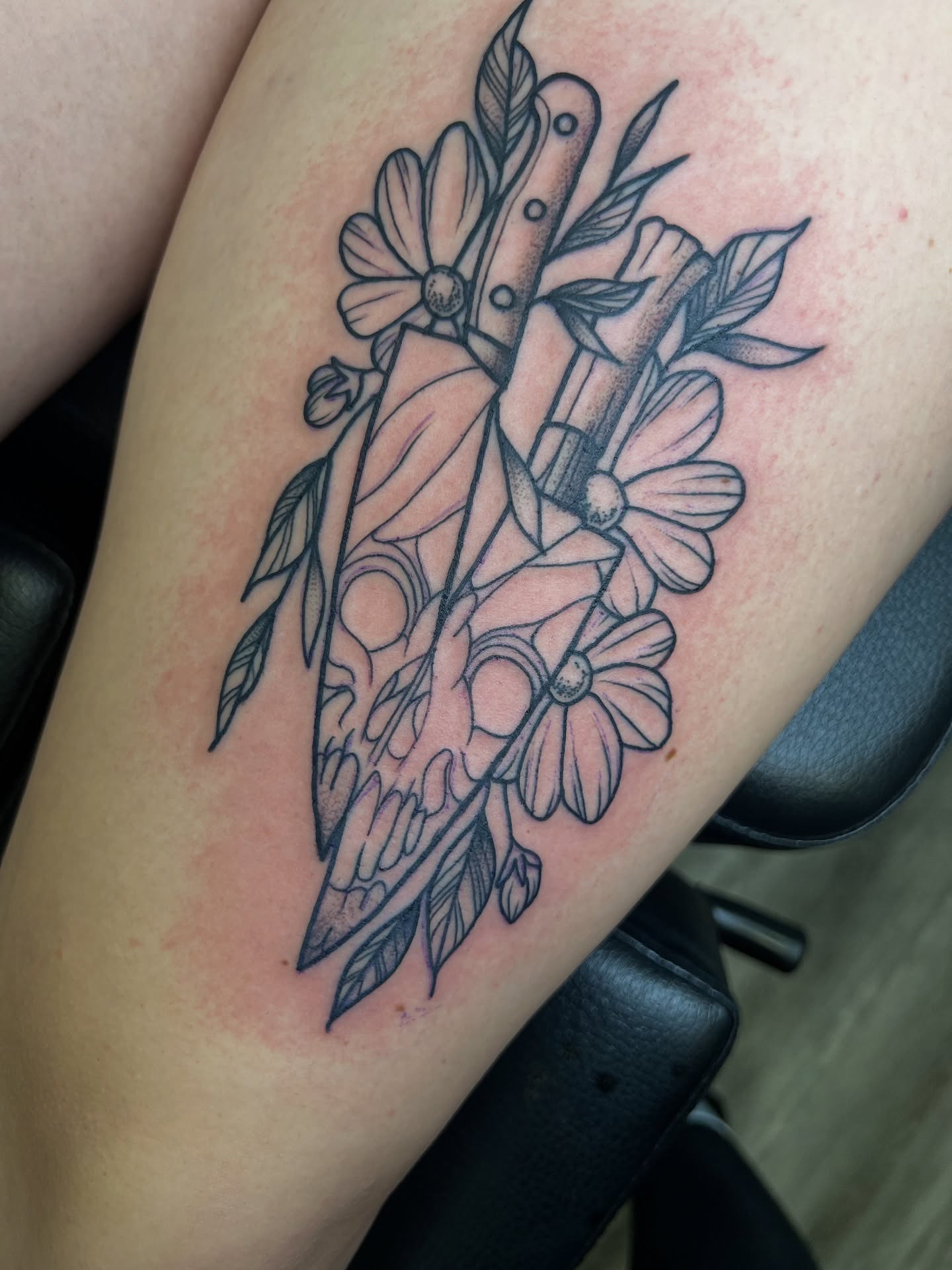 Skull and flowers black and grey tattoo on the thigh by Tattoo Artist