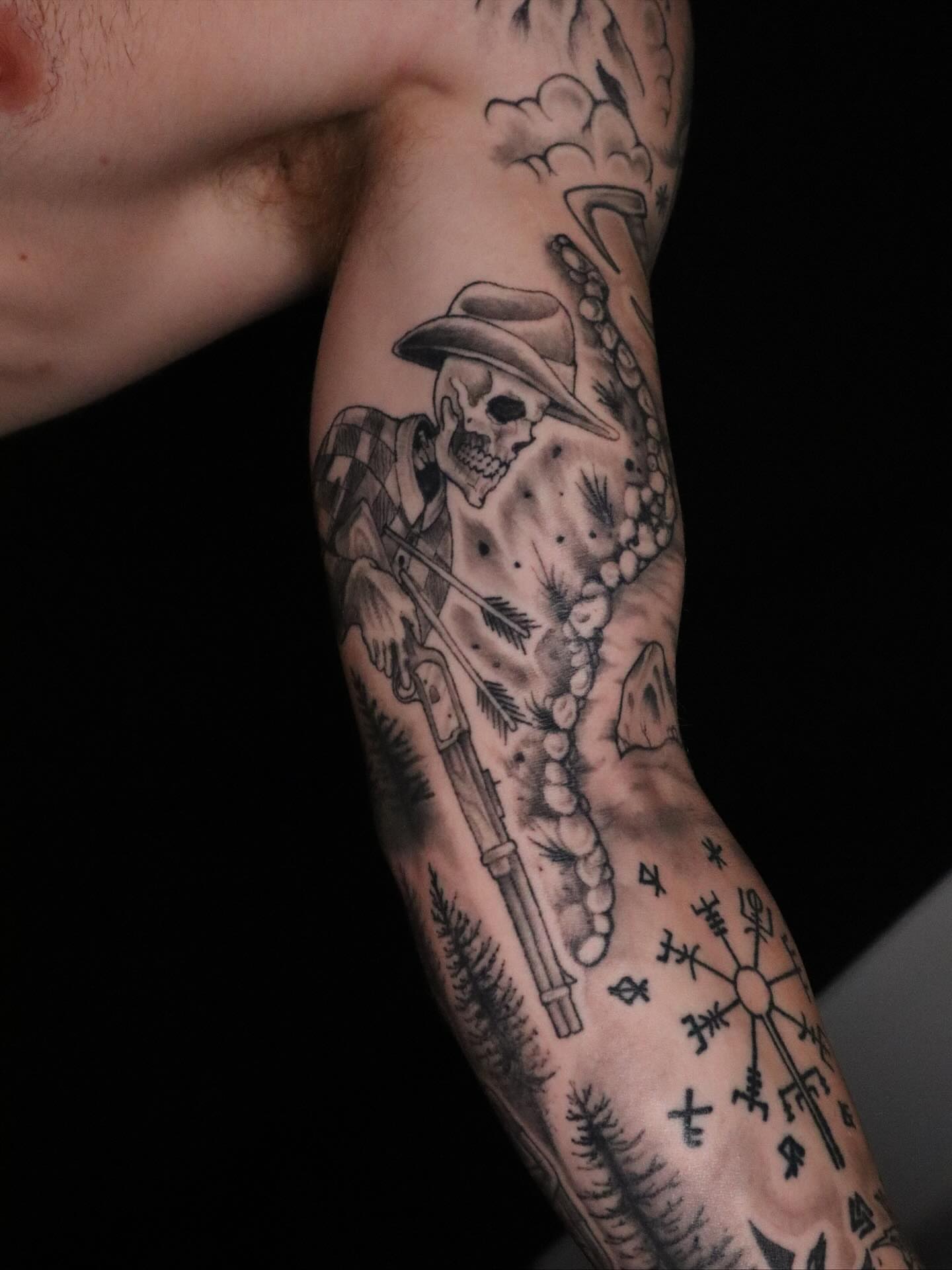 Skull with rifle black and grey tattoo on the forearm by Brandon Seven