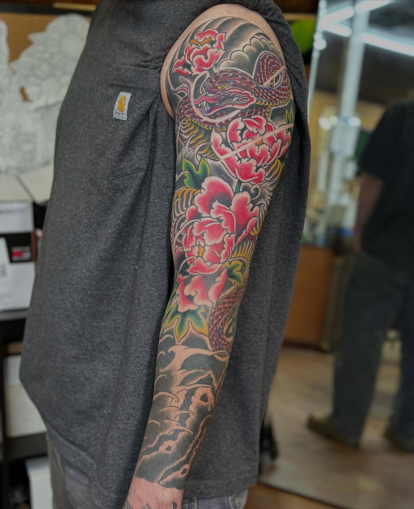 Snake and peony American traditional tattoo on the upper arm by Wesley Lam