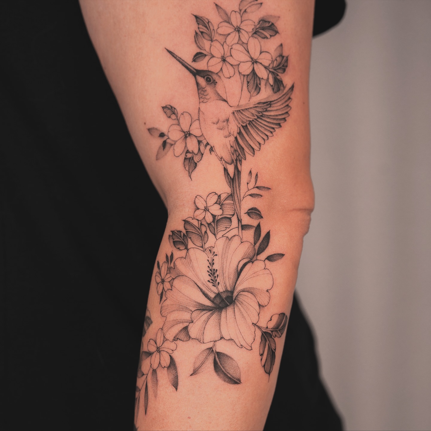 Hummingbird and flowers black and grey tattoo on the forearm by Leo Gao