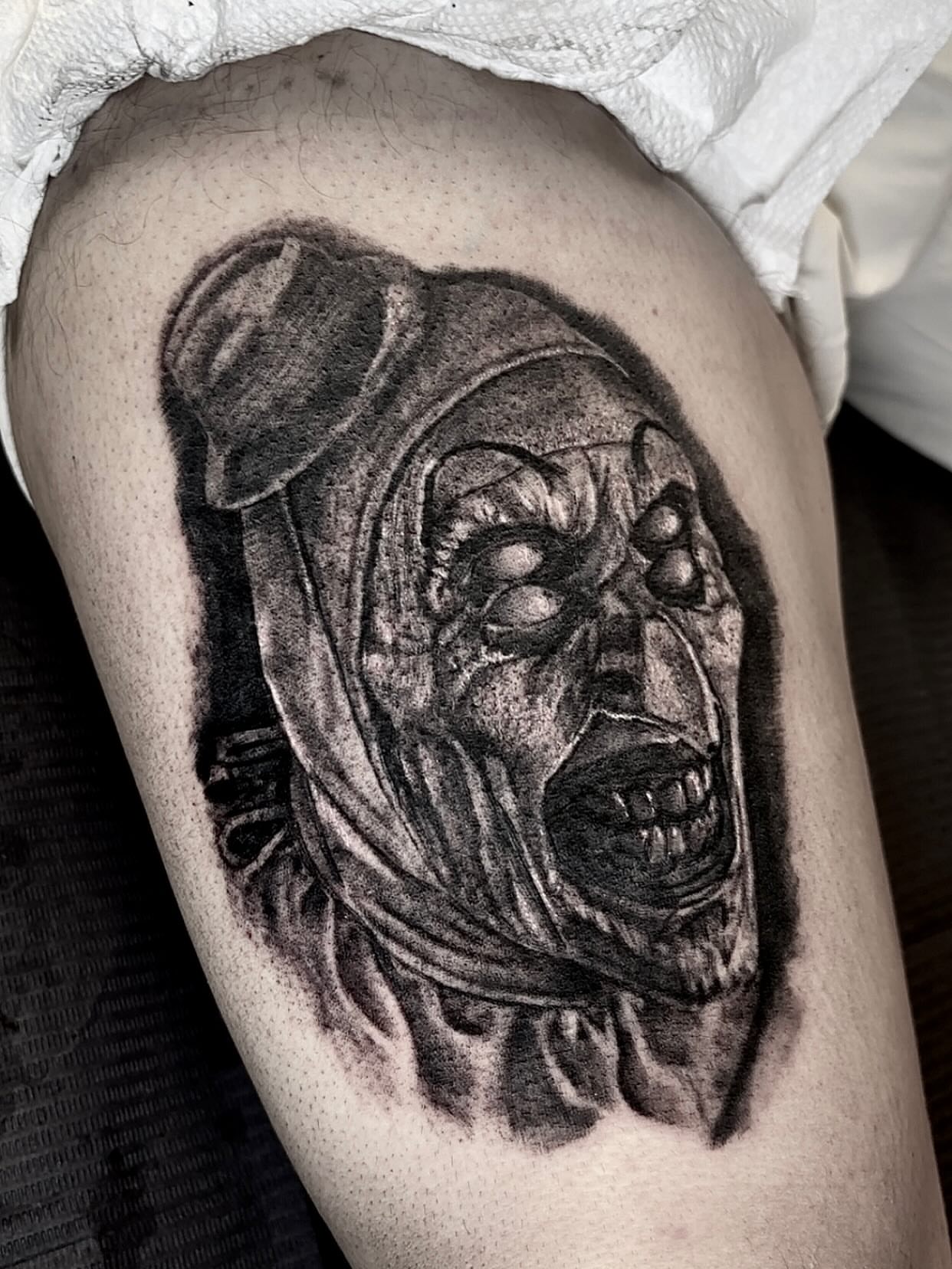 Clown mask realism tattoo on the thigh by Dre Ortiz