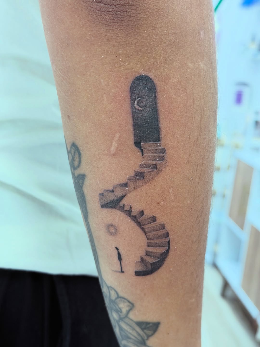 Staircase to a door with moon surrealism tattoo on the forearm by Ink About Me - Amanda’s Fine Lines