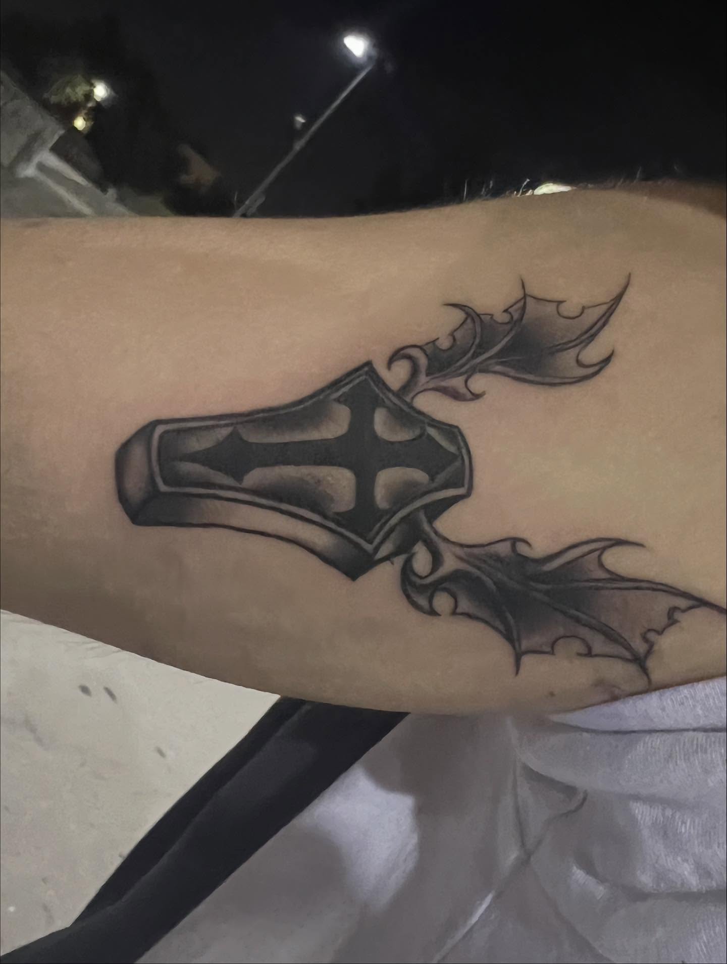 Cross with bat wings black and grey tattoo on the forearm by zion