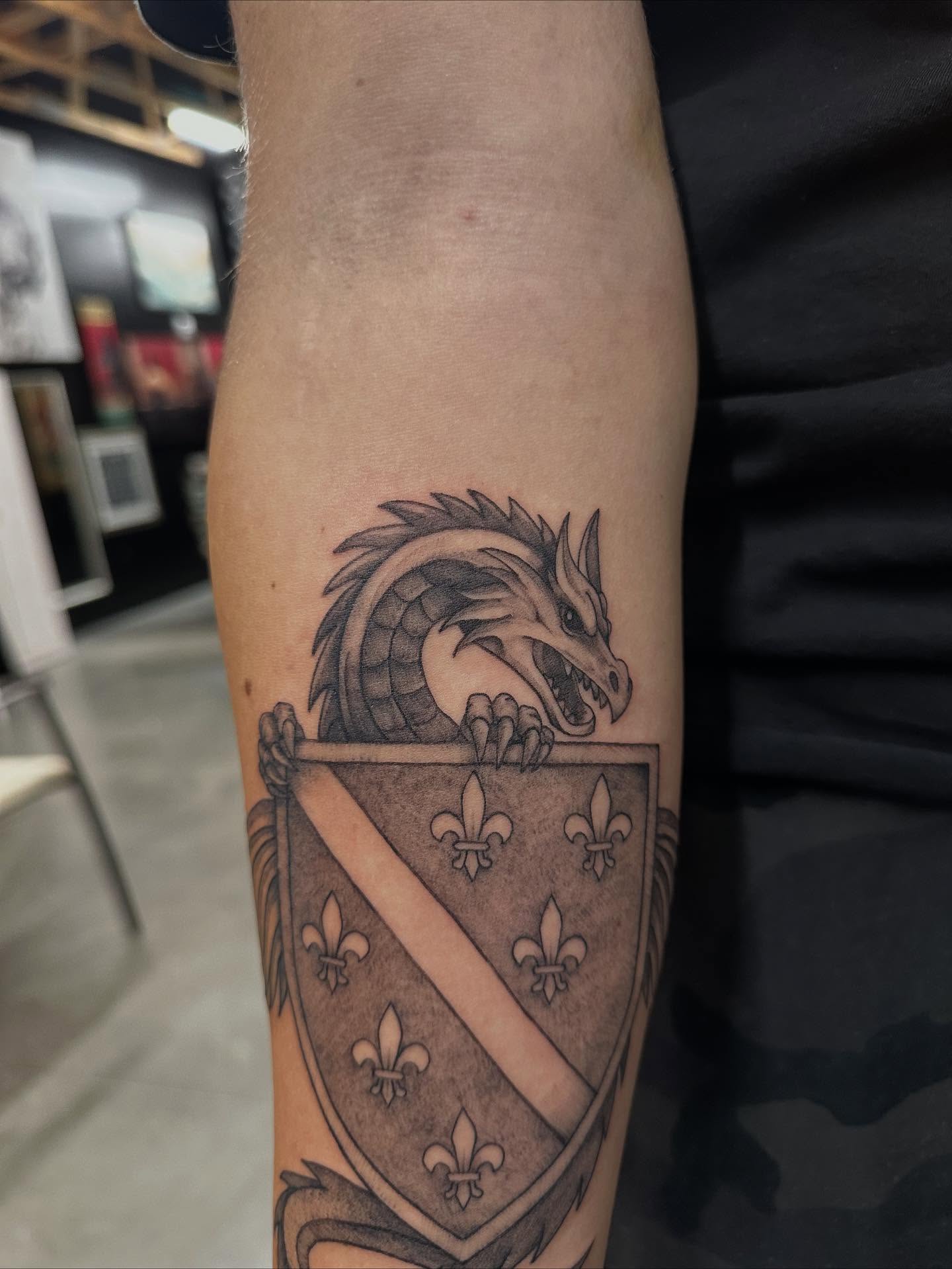 Dragon and shield black and grey tattoo on the forearm by Galen Thornburg