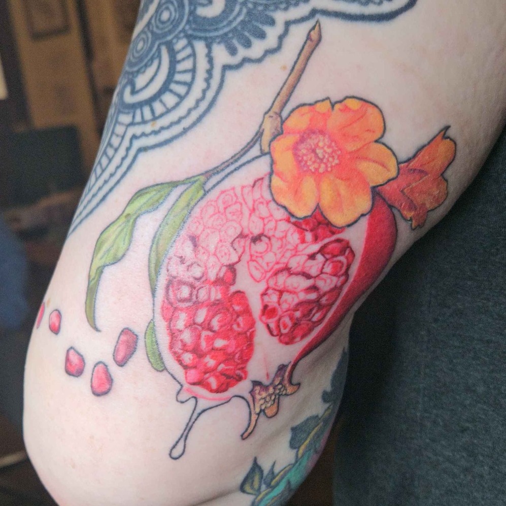 Pomegranate and flower realism tattoo on the forearm by Iram Withencroft