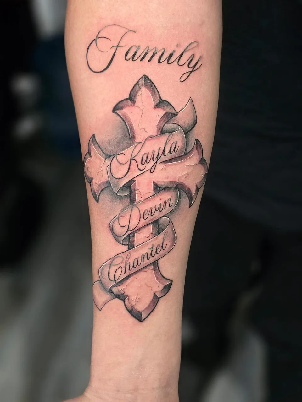 Cross with family names black and grey tattoo on the forearm by Eldaddy