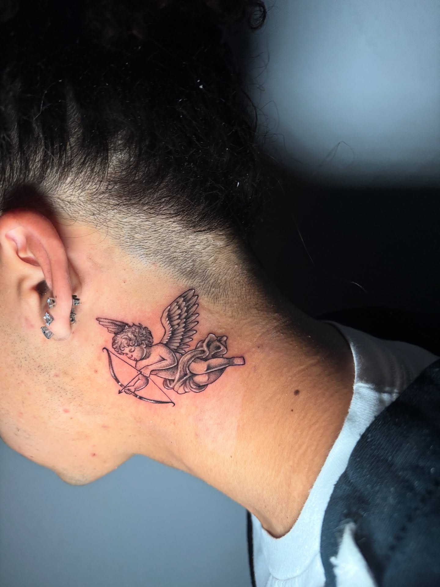 Cherub with bow and arrow black and grey tattoo on the neck by 𝕸𝖔𝖓𝖎𝖖𝖚𝖊𝖊𝖓